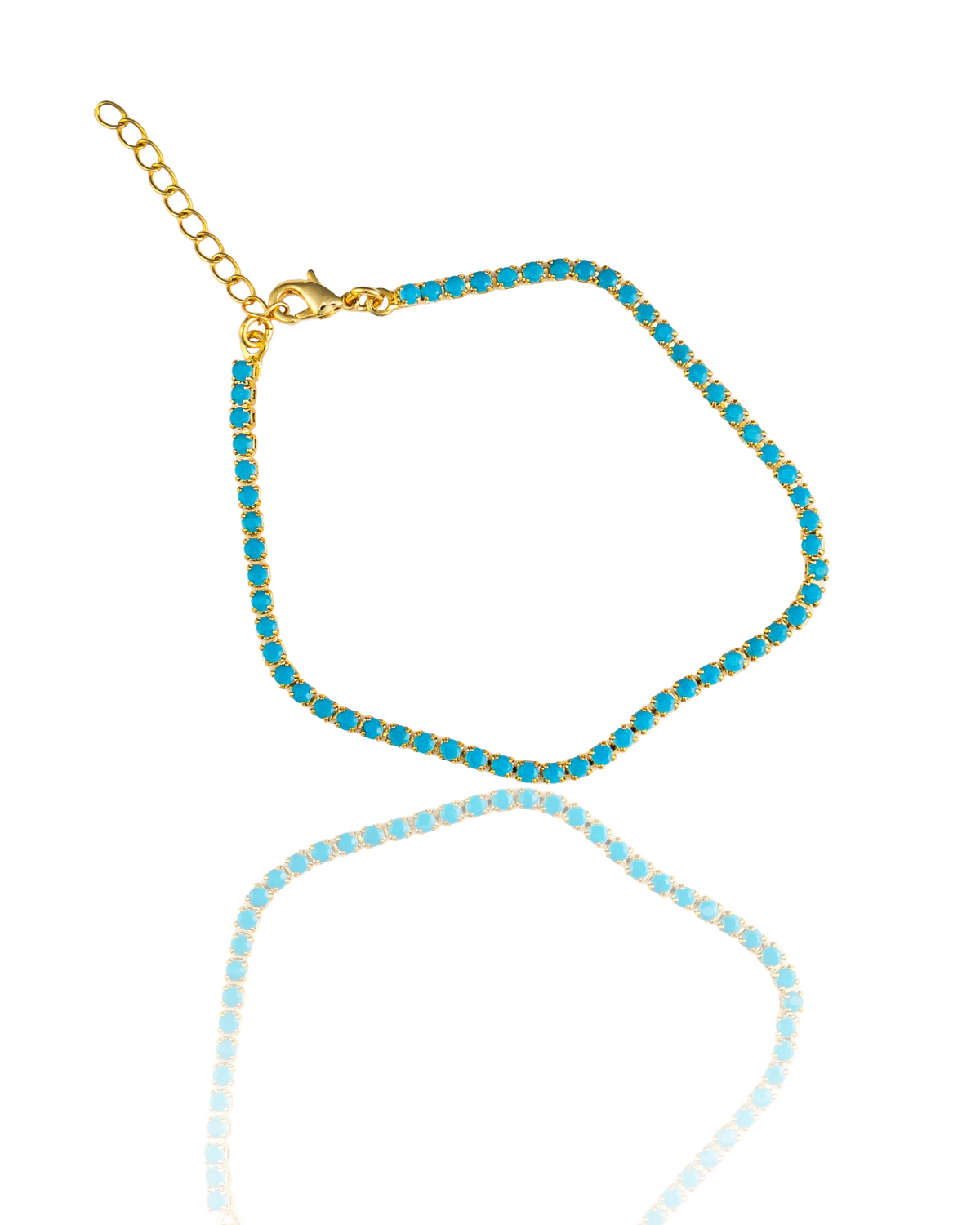 A gold tennis bracelet embedded with vibrant turquoise stones rests on a reflective white surface, displaying its lobster clasp and adjustable extension chain.