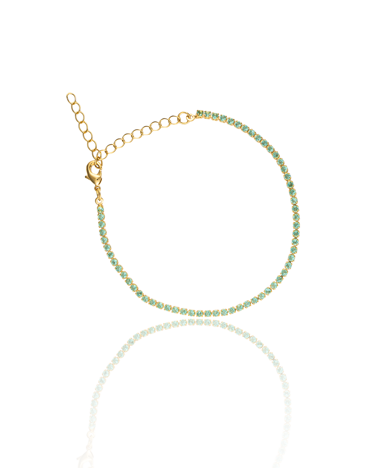 A delicate gold tennis bracelet sparkles with small green gemstones and features an adjustable chain clasp against a white background.