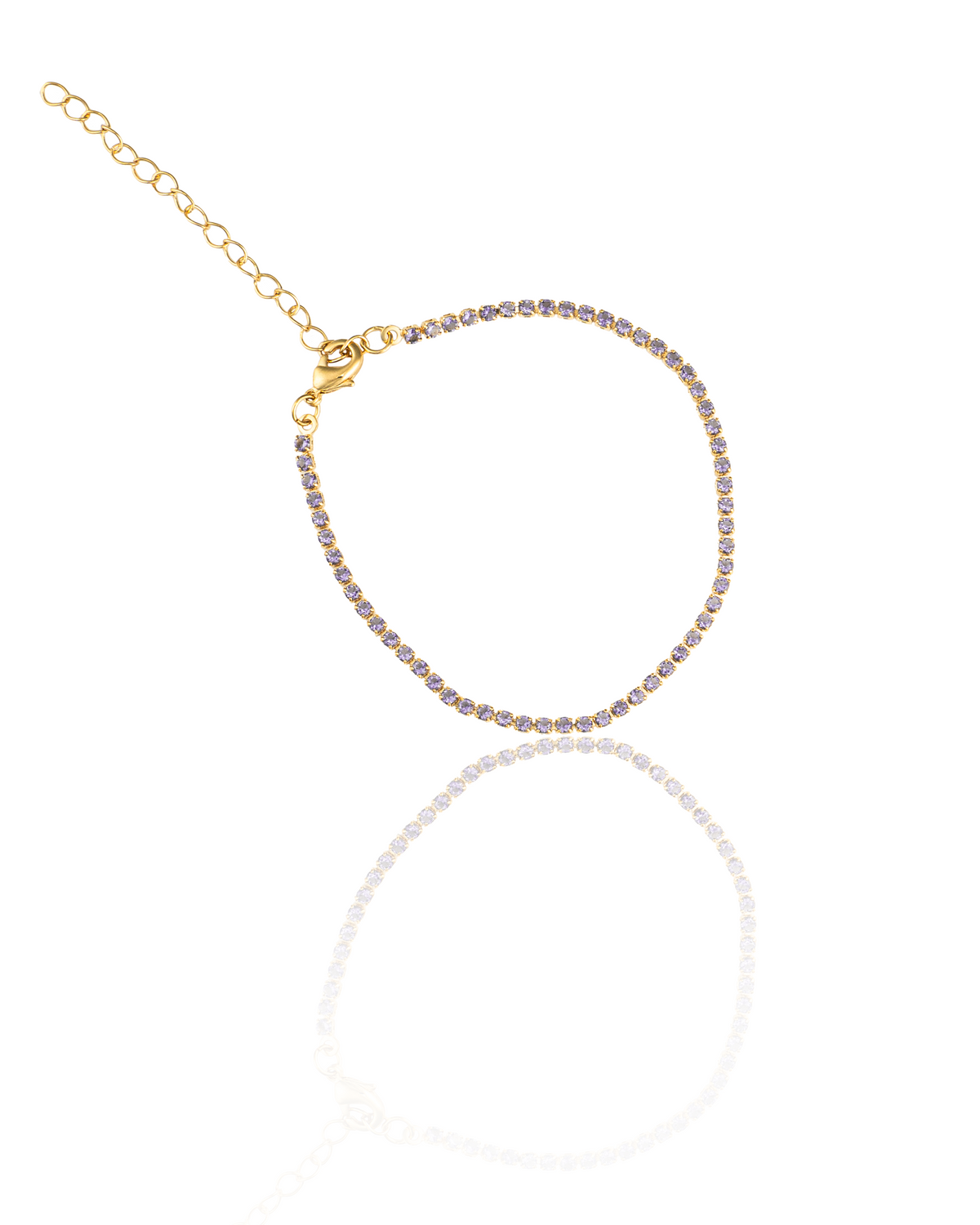 A delicate gold tennis bracelet studded with sparkling purple stones displays its clasp and extender chain against a white background with a subtle reflection.