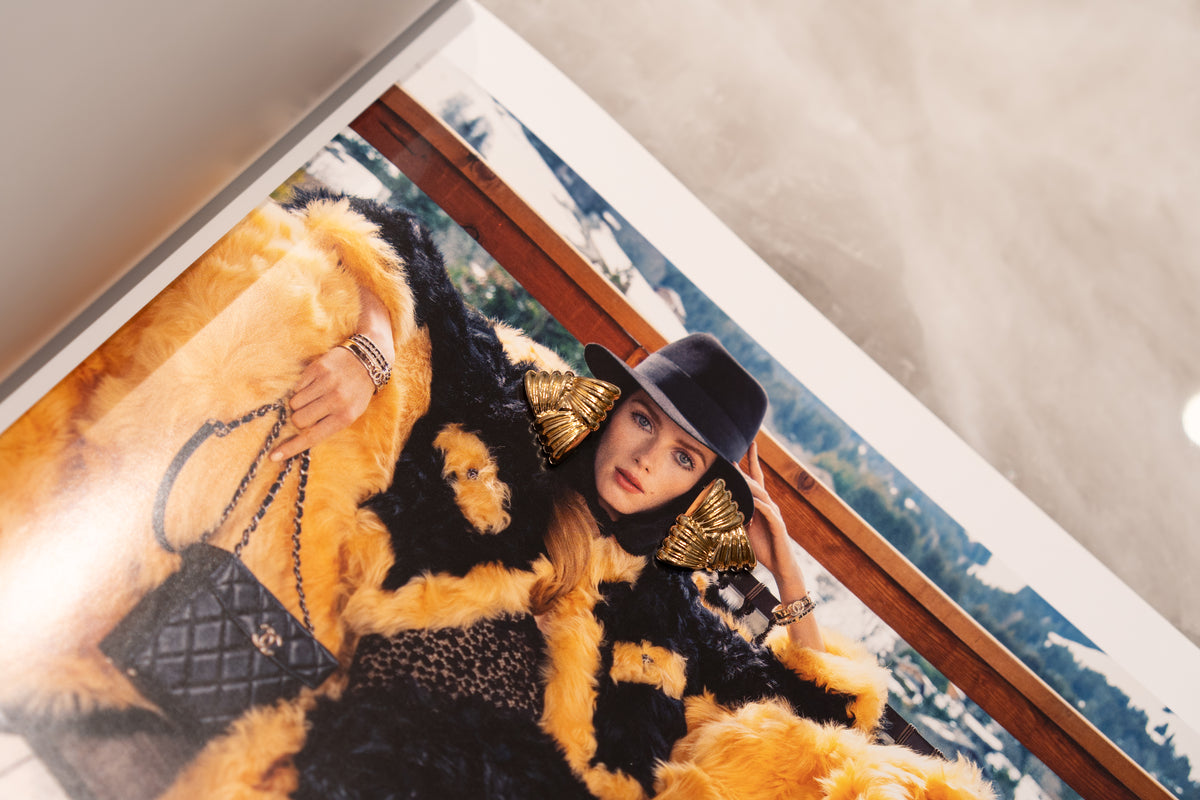 A fashion magazine page features a model wearing a black hat, statement gold earrings, and a luxurious yellow and black faux fur coat while holding a quilted Chanel handbag.