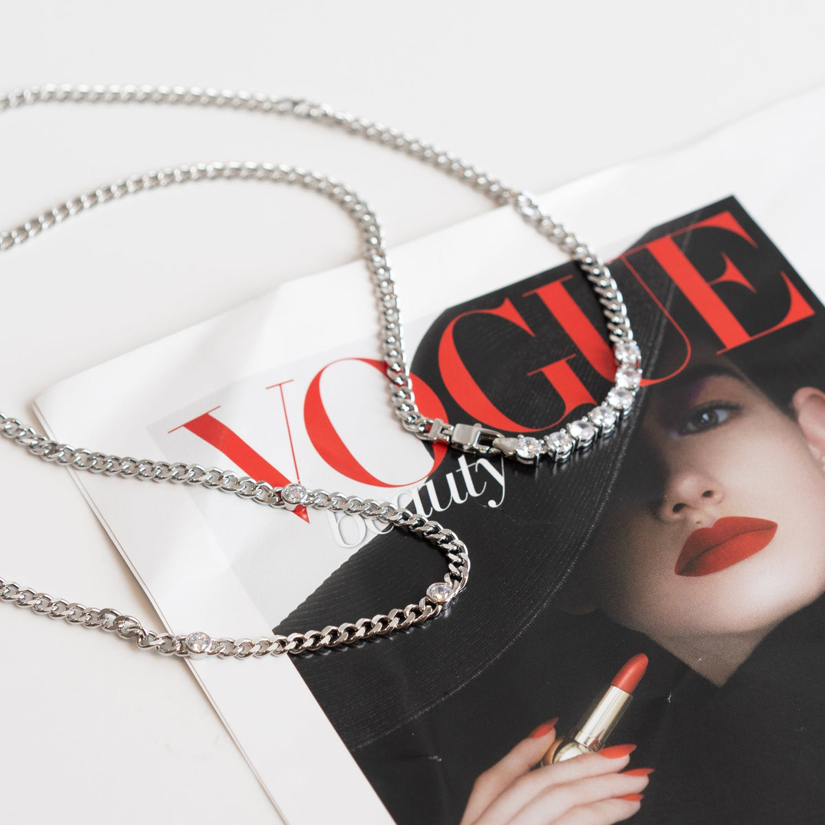 A delicate silver chain necklace rests gracefully across the glossy cover of a Vogue magazine.