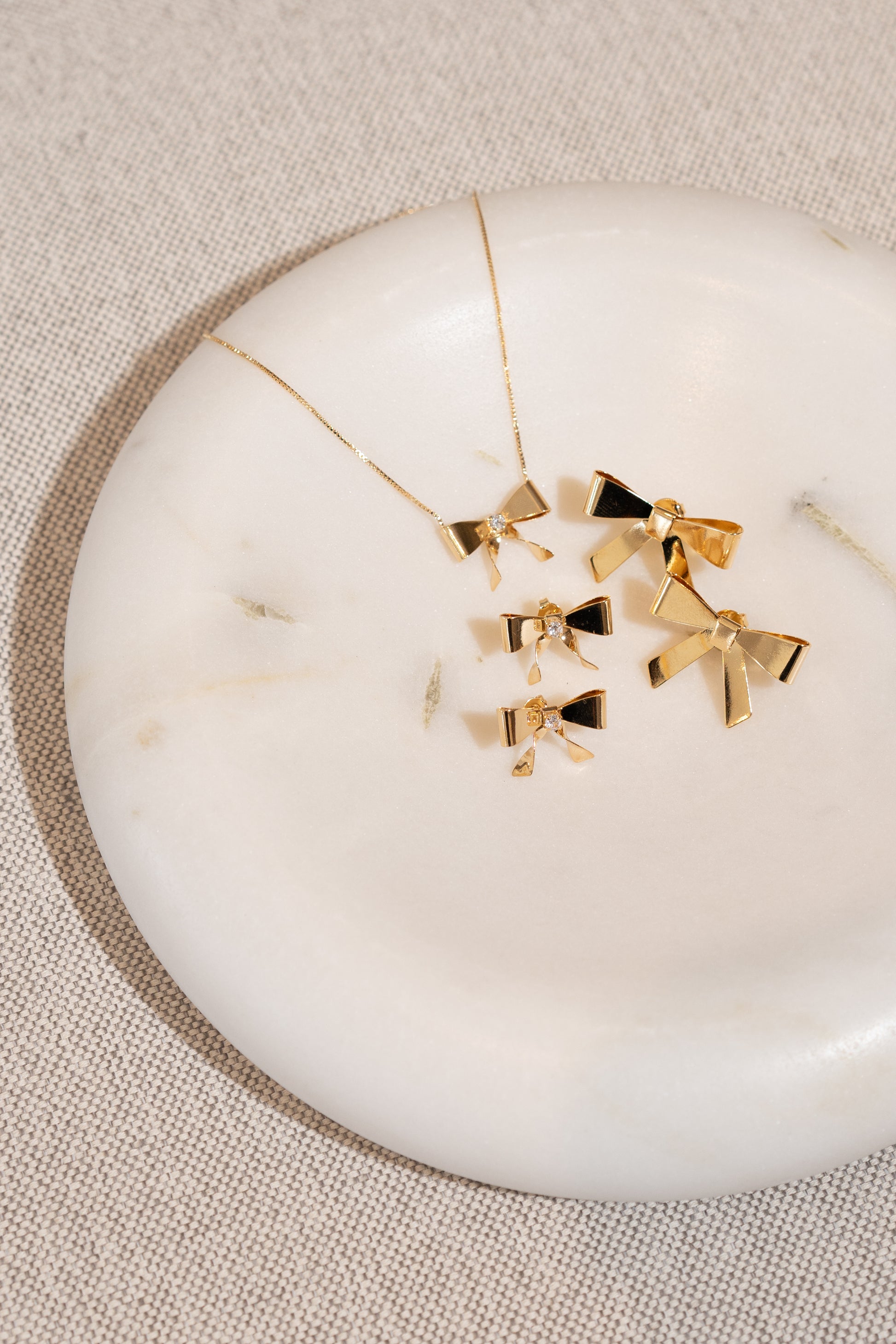 A matching gold jewelry set featuring bow-shaped necklaces and earrings rests elegantly on a white marble tray.