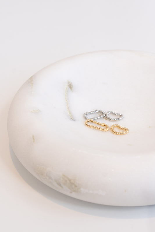 Two gold and two silver twisted huggie hoop earrings rest on a white marble jewelry dish.