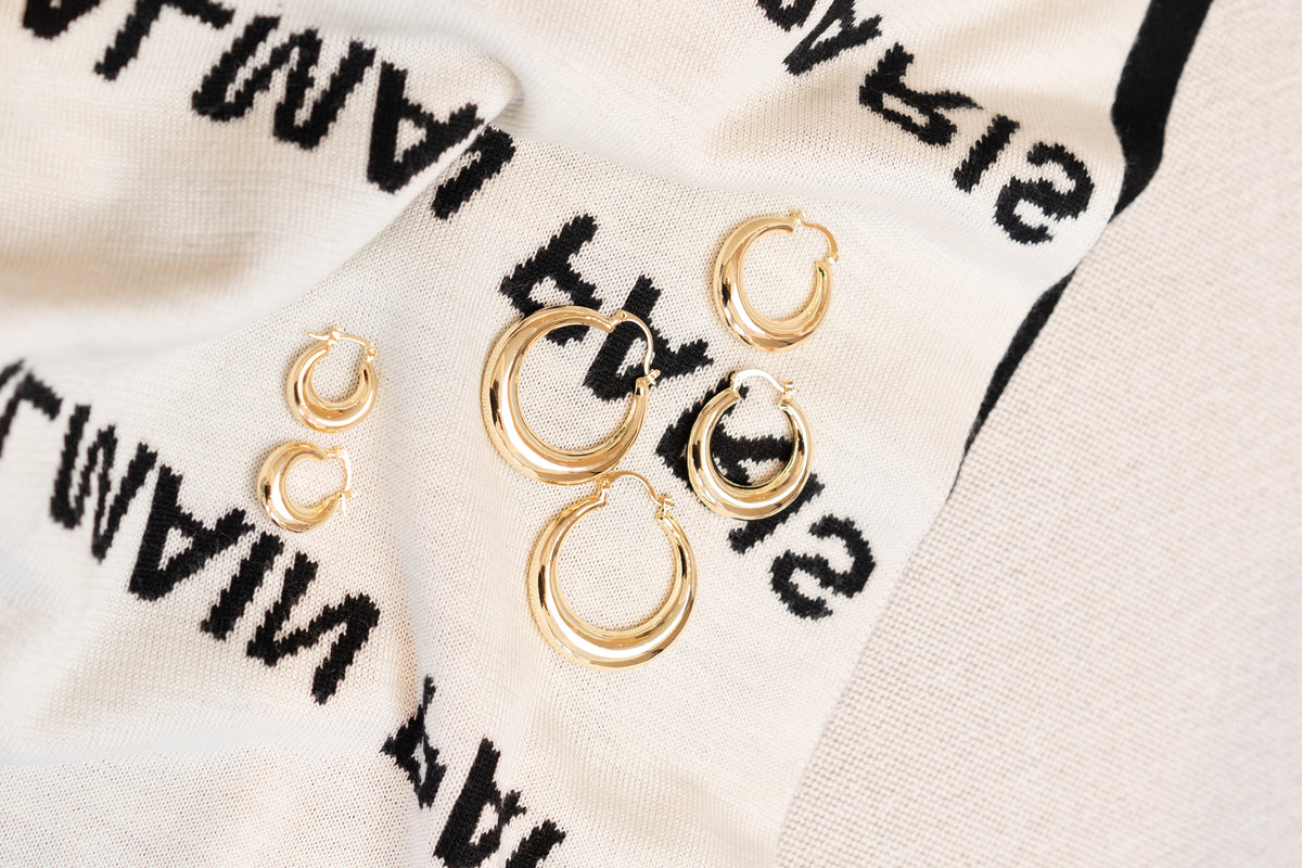 A collection of polished gold hoop earrings in varying sizes rests on a textured white and black patterned fabric.