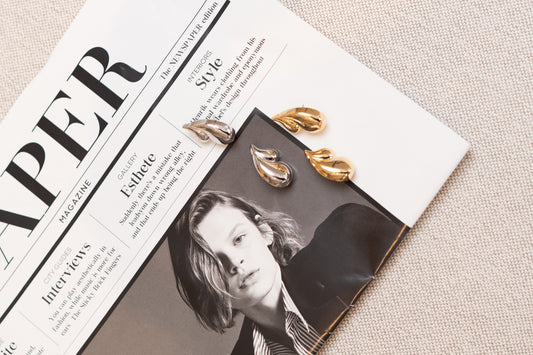 Two pairs of sleek gold and silver teardrop earrings rest artfully on an open fashion magazine.