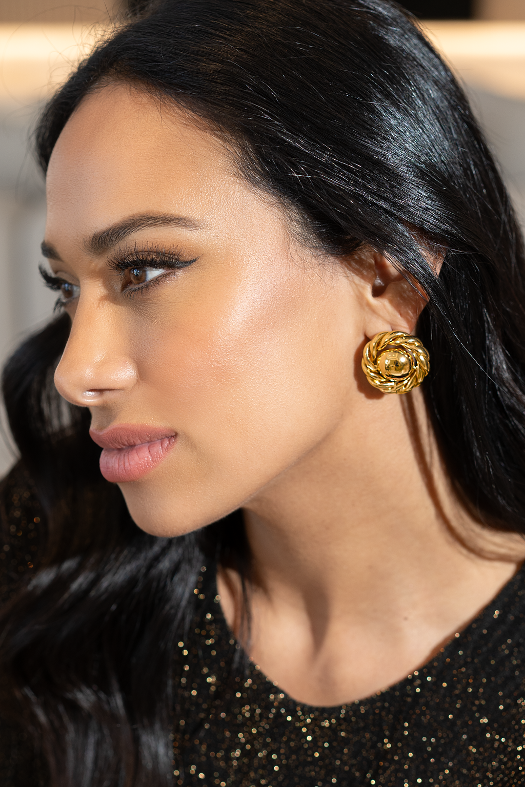 A glamorous woman wearing textured gold button earrings gazes thoughtfully in profile.