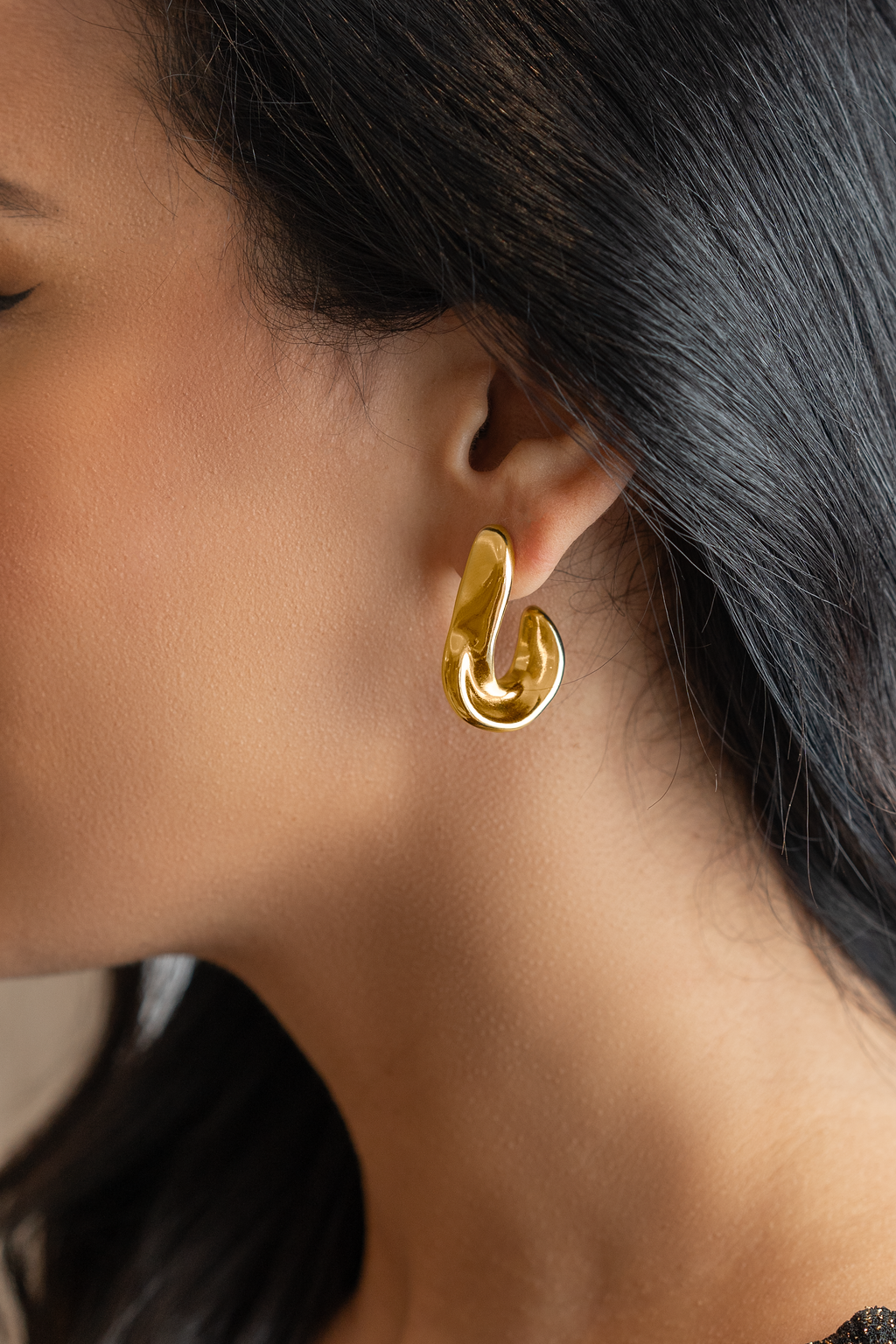 A woman wearing a glossy, abstract gold sculptural earring on her earlobe.