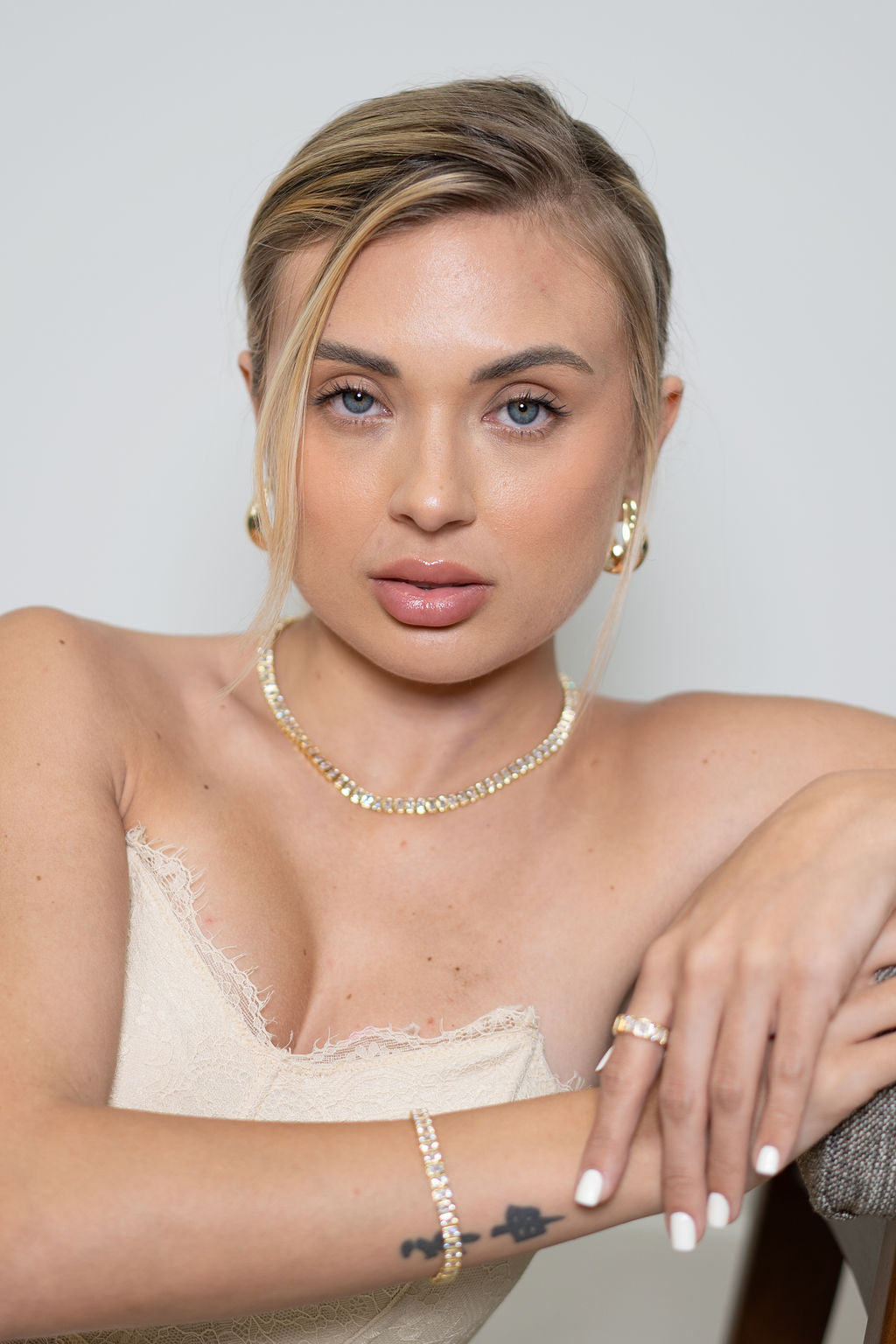 A blonde woman with blue eyes wears a sparkling tennis necklace, matching earrings, and a delicate bracelet while posing elegantly.