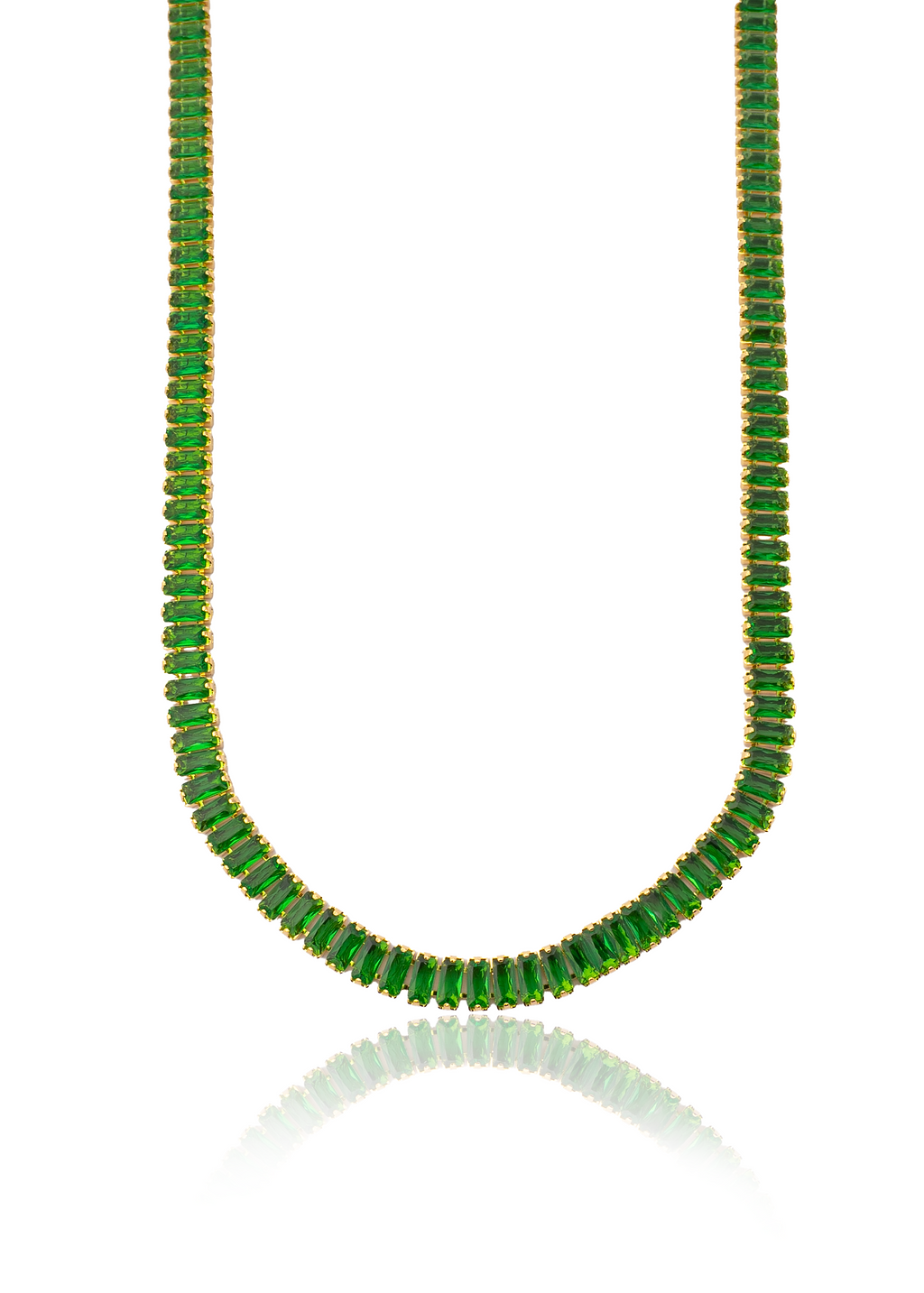 A gold tennis necklace featuring vibrant green emerald-cut gemstones drapes gracefully against a white background, casting a soft reflection below.