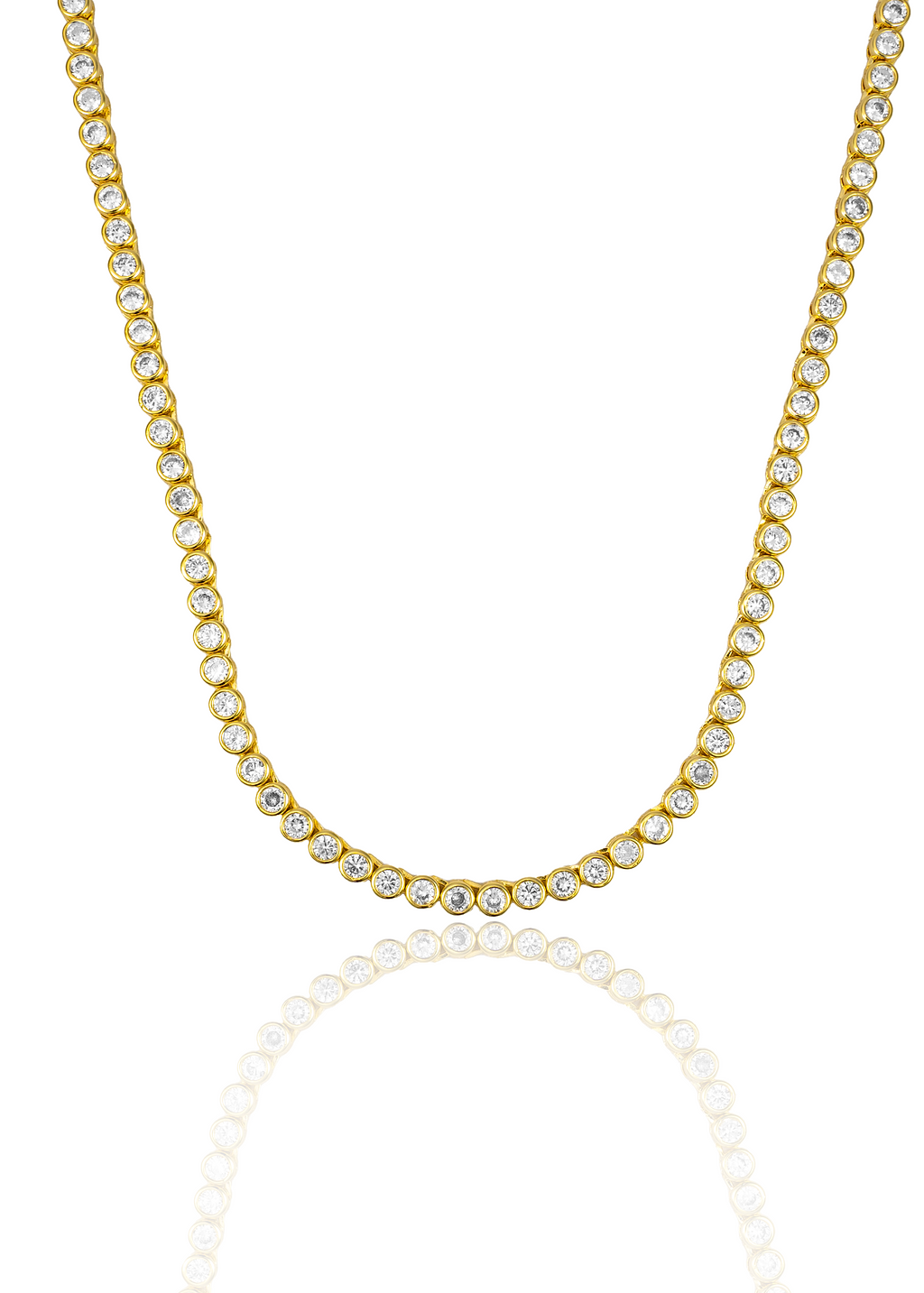 A gold bezel-set diamond tennis necklace rests against a white background, casting a soft reflection below.