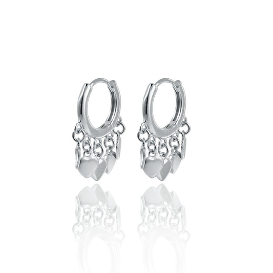 A pair of silver hoop earrings adorned with dangling heart charms and delicate chains rests on a reflective white surface.