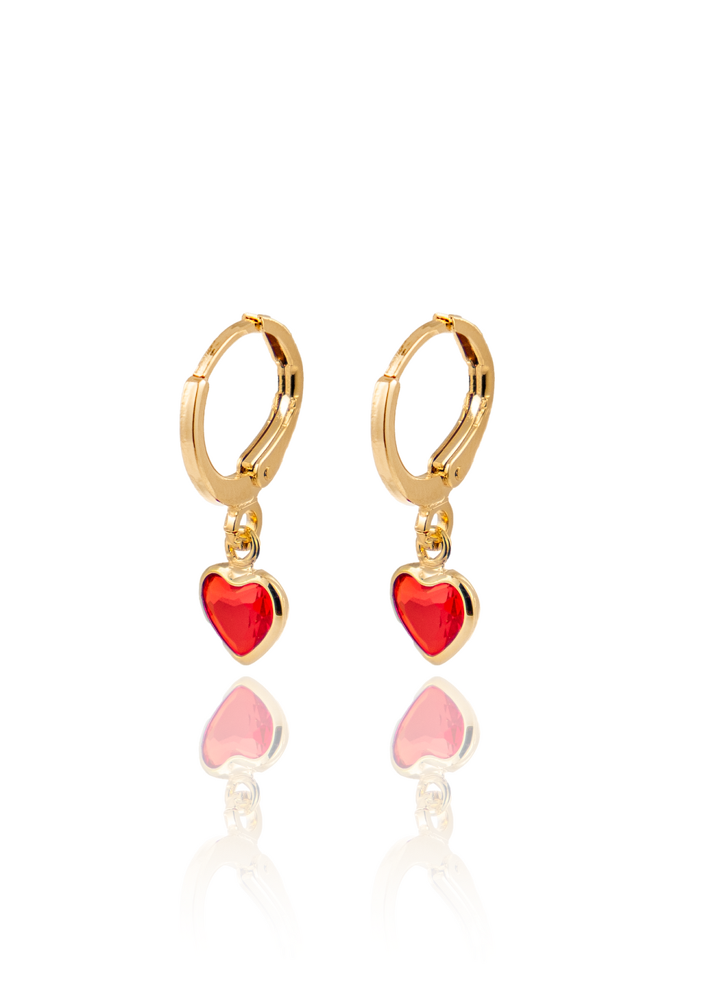 A pair of gold huggie hoop earrings features dangling red heart charms against a white background.