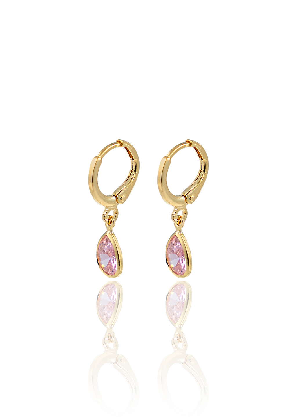 A pair of gold huggie hoop earrings with dangling teardrop-shaped pink cubic zirconia stones rests on a reflective white surface.