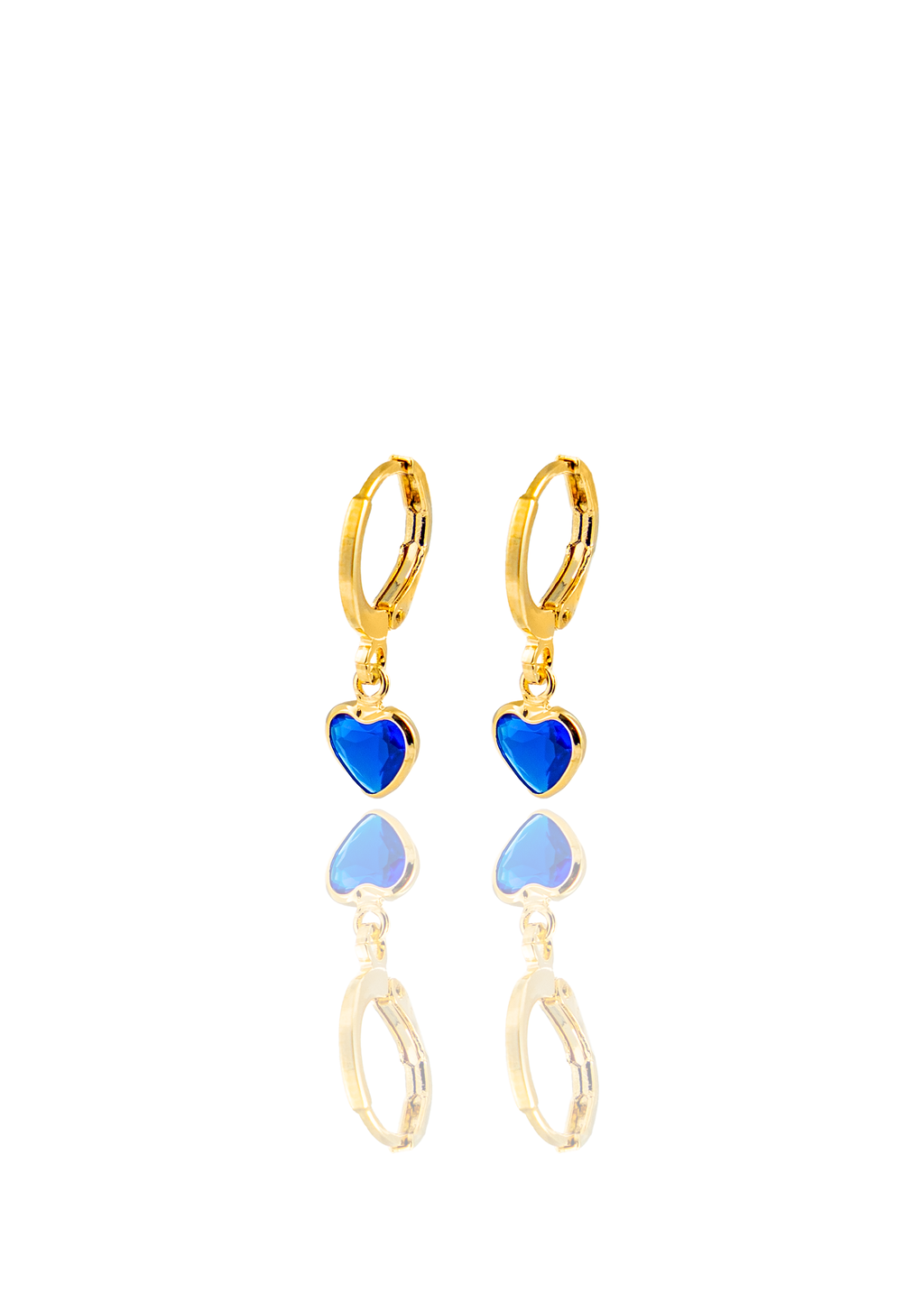 A pair of gold hoop earrings featuring dangling blue heart-shaped charms rest against a reflective white surface.