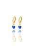 A pair of gold hoop earrings featuring dangling blue heart-shaped charms rest against a reflective white surface.