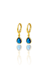 A pair of elegant gold hoop earrings featuring dangling teardrop-shaped blue gemstones displayed against a white background.