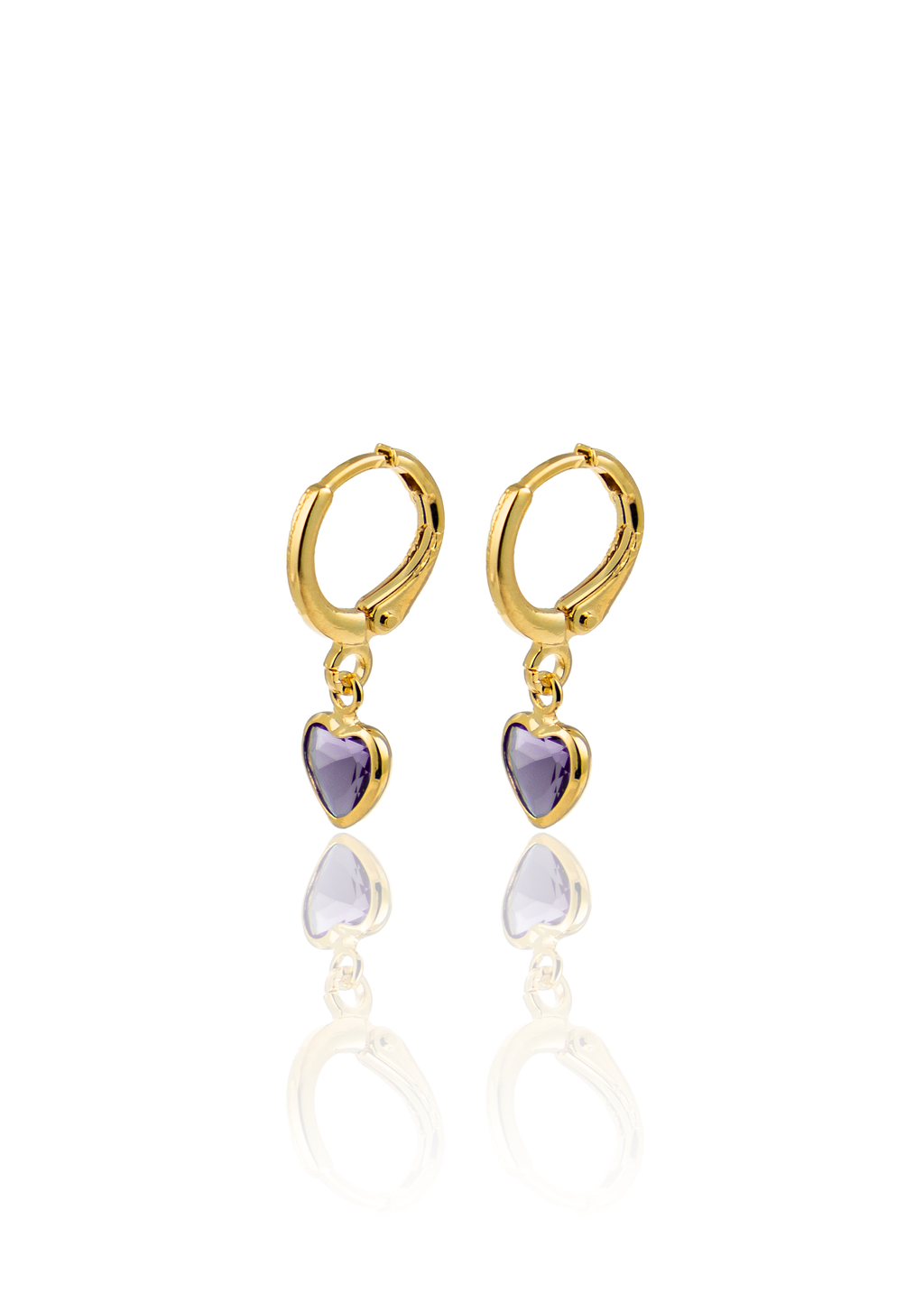 A pair of gold huggie hoop earrings featuring dangling purple heart-shaped gemstones reflects on a white surface.
