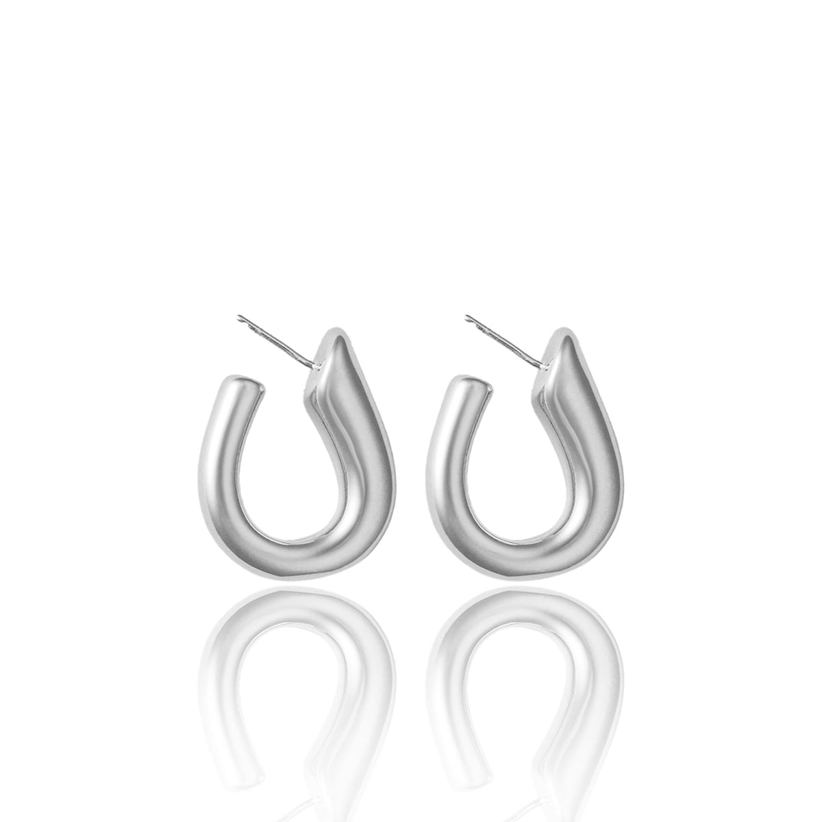 A pair of chunky silver hoop earrings rests on a reflective white surface.