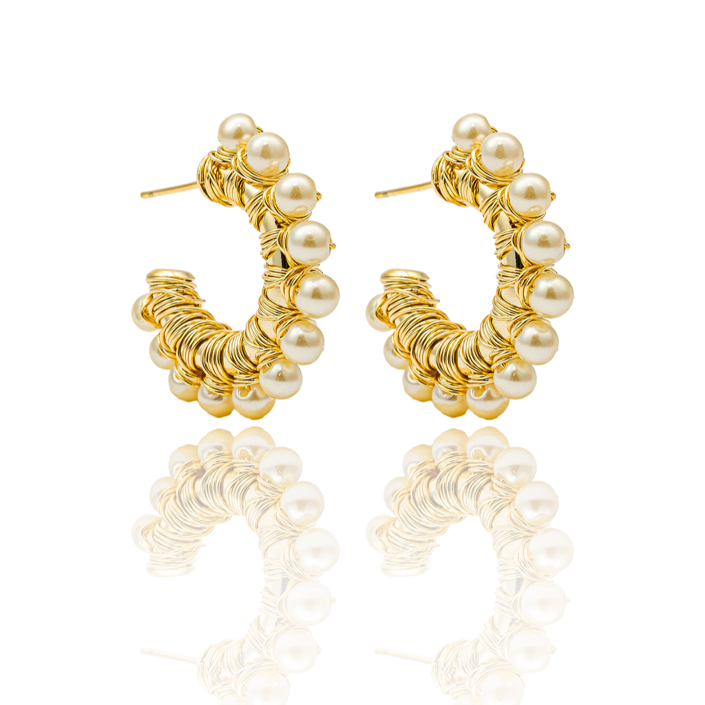 A pair of elegant gold wire-wrapped hoop earrings adorned with lustrous pearls rests against a white background, casting a soft reflection below.