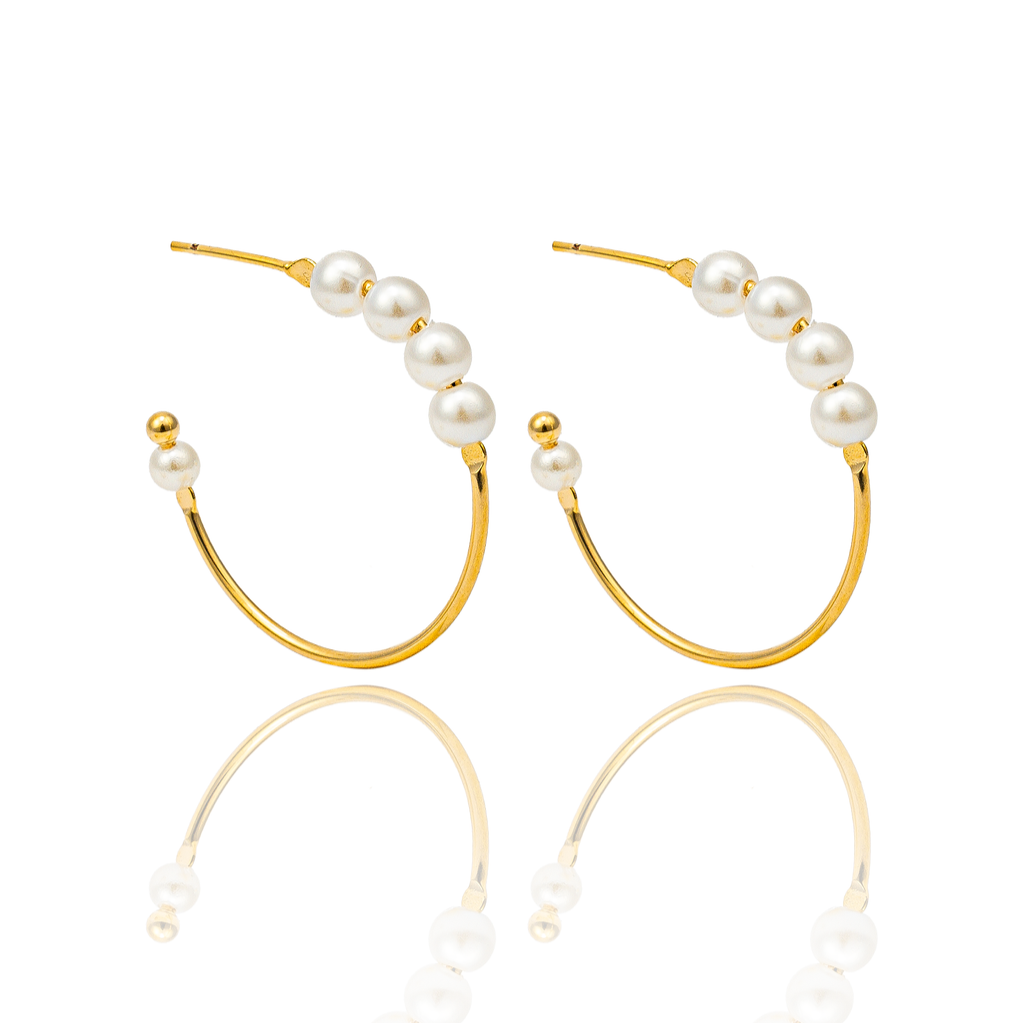 A pair of elegant gold hoop earrings embellished with ascending white pearls sits against a clean white background, reflecting softly on the glossy surface below.
