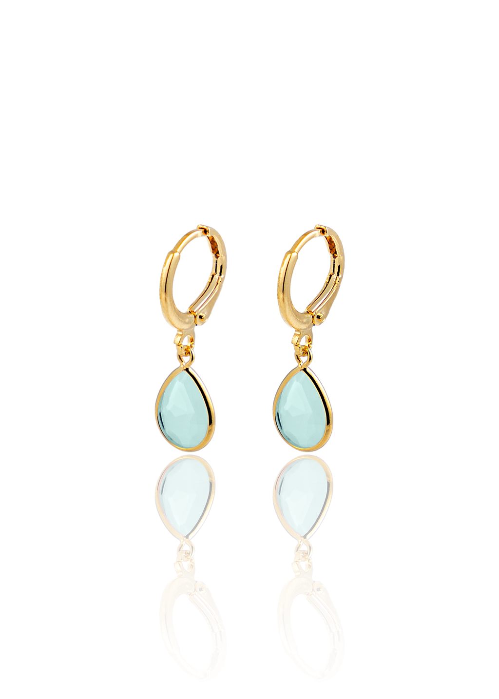 A pair of gold huggie hoop earrings featuring dangling teardrop-shaped light blue gemstone charms rests on a white reflective surface.