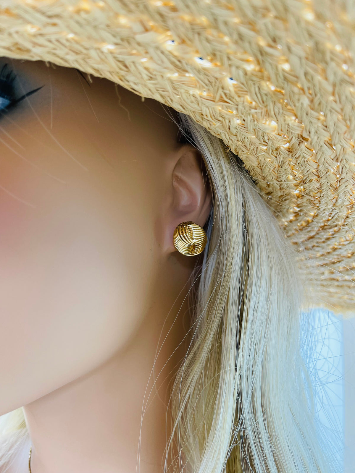 A blonde mannequin wearing a textured gold dome earring and a straw sun hat.
