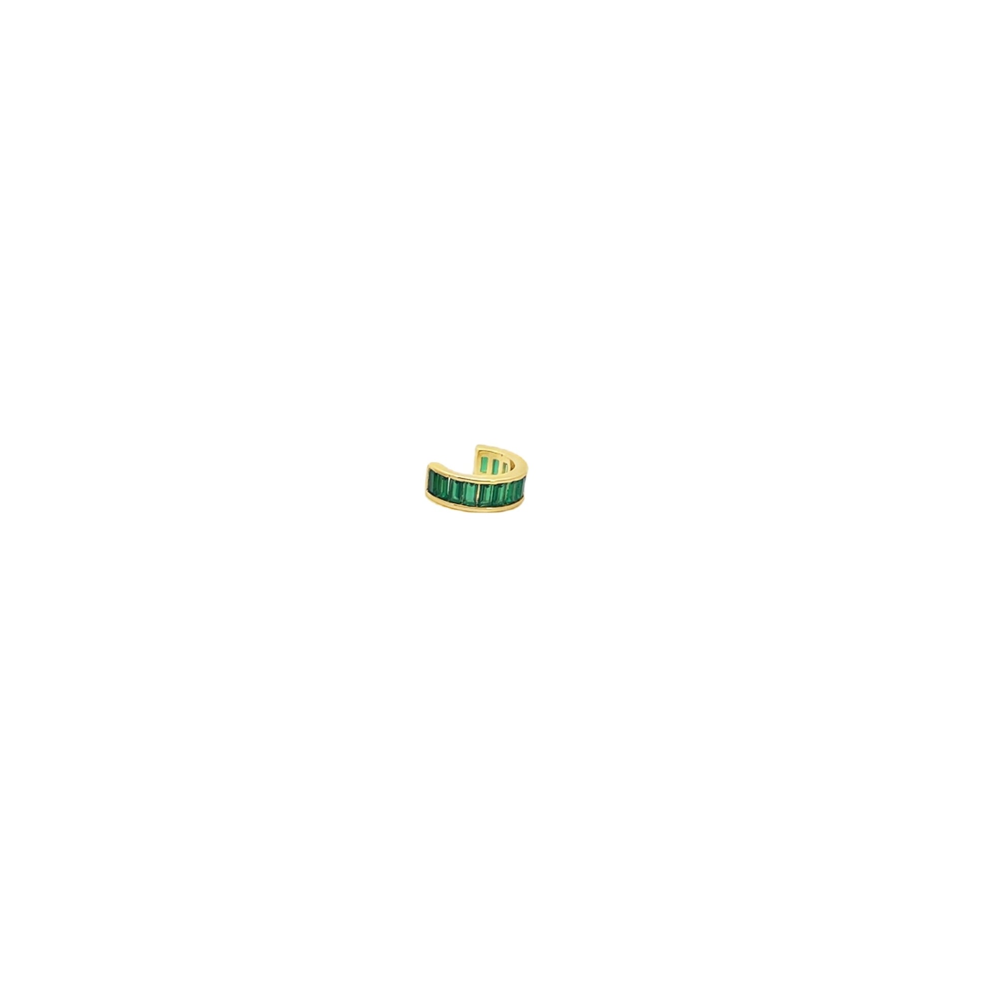 A gold ear cuff featuring vibrant green baguette-cut stones rests against a clean white background.