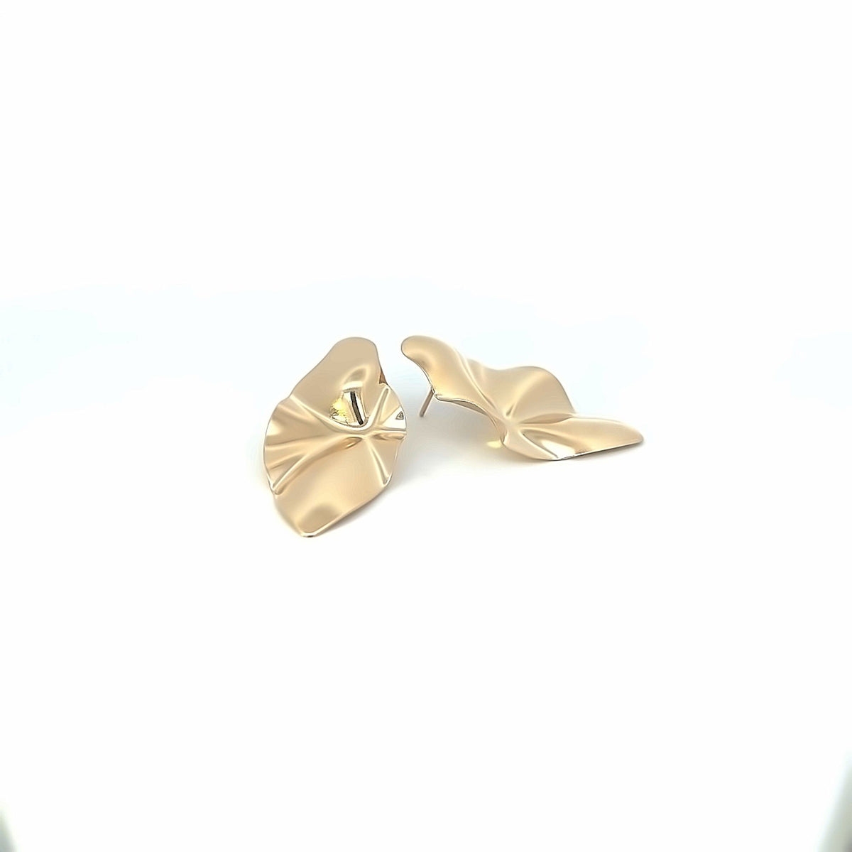 A pair of abstract gold leaf-shaped stud earrings rest against a clean white background.