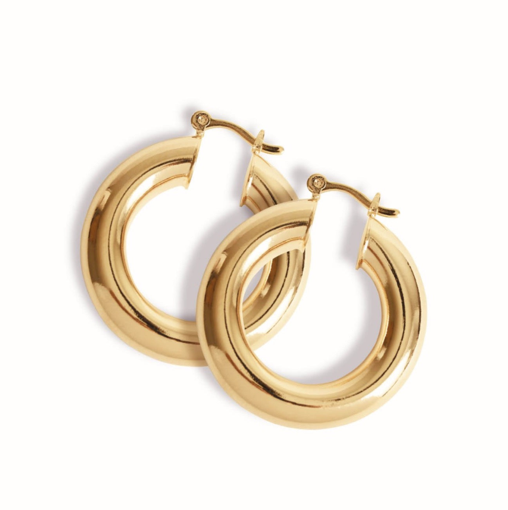 A pair of polished thick gold hoop earrings rests against a white background.