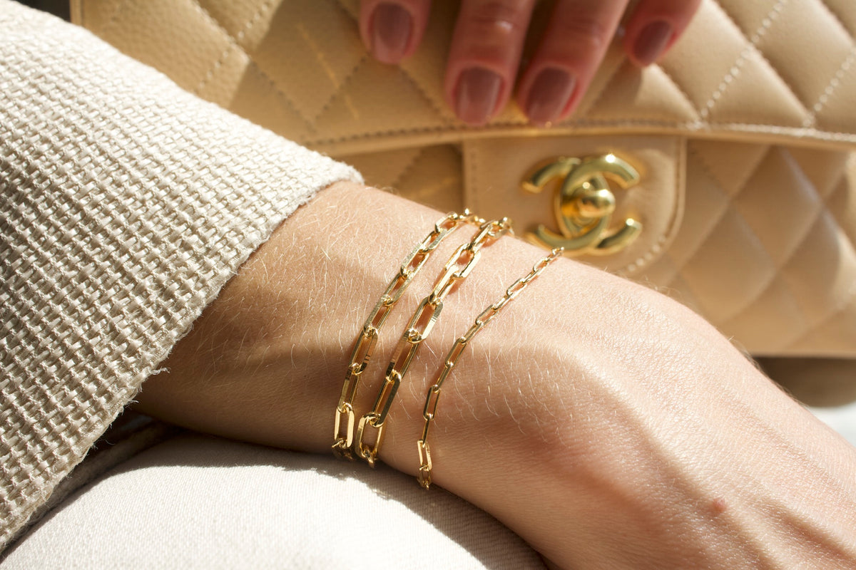 A woman wears a stack of delicate gold chain bracelets on her wrist near a quilted designer handbag.