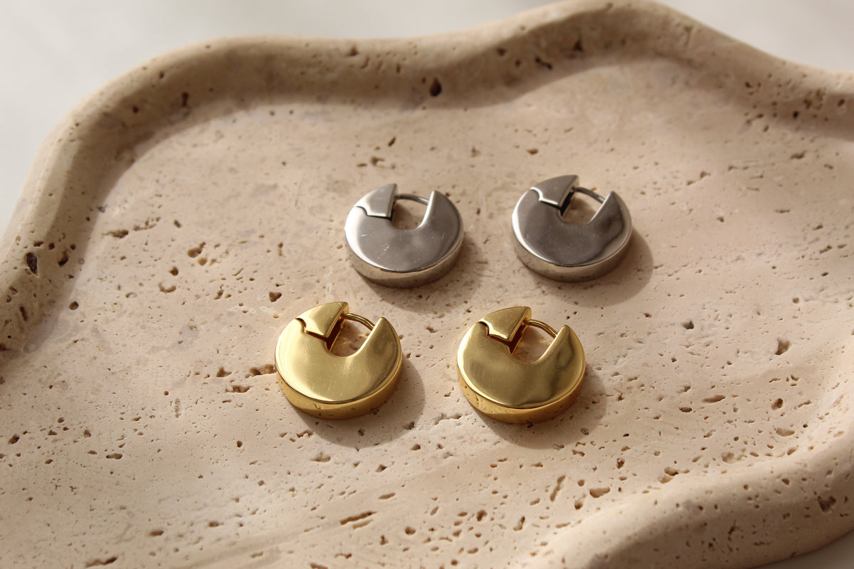 A pair of gold and a pair of silver chunky hoop earrings rest on a textured beige tray.