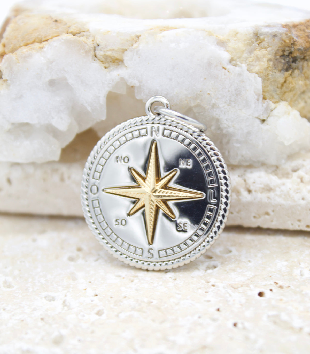 A detailed silver compass pendant with a gold star center rests against a textured white crystal background.