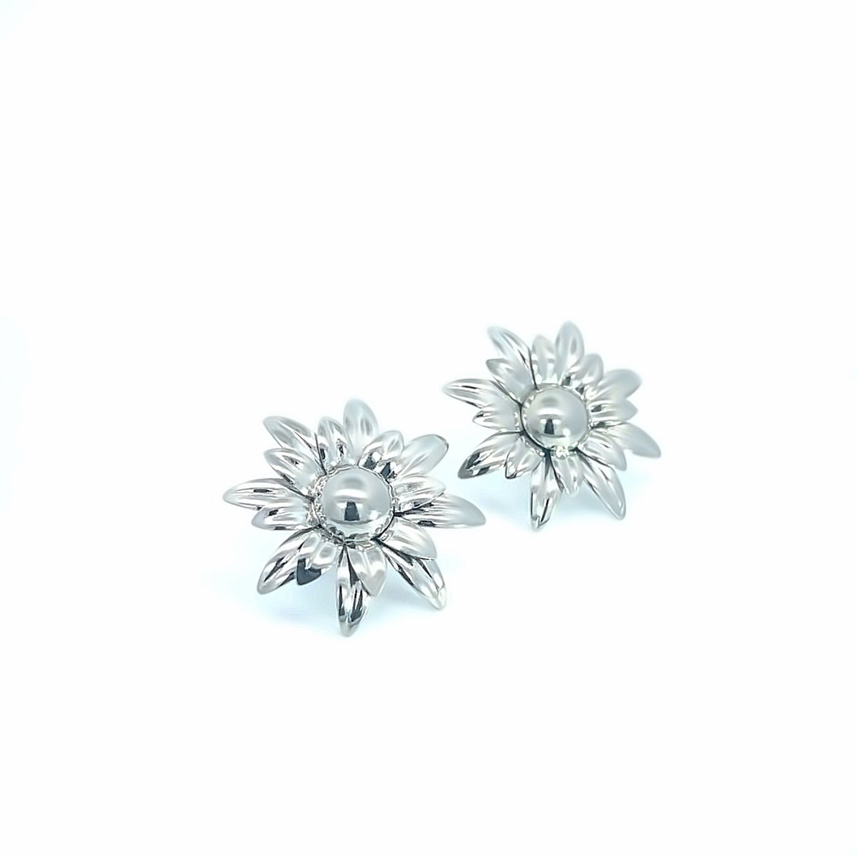 A pair of shiny silver flower-shaped stud earrings rests against a clean white background.