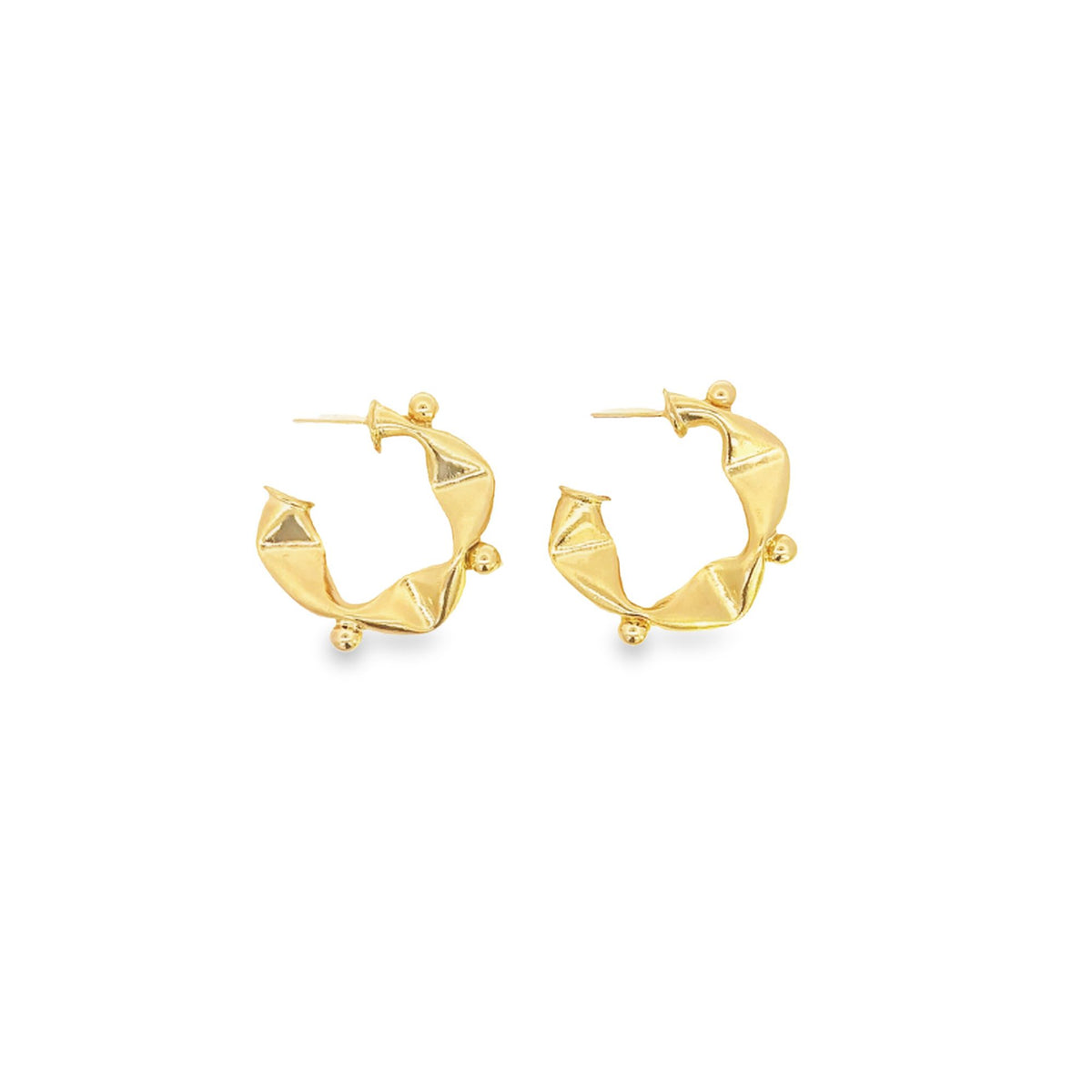A pair of sculptural gold hoop earrings with textured faceted details rests on a white background.