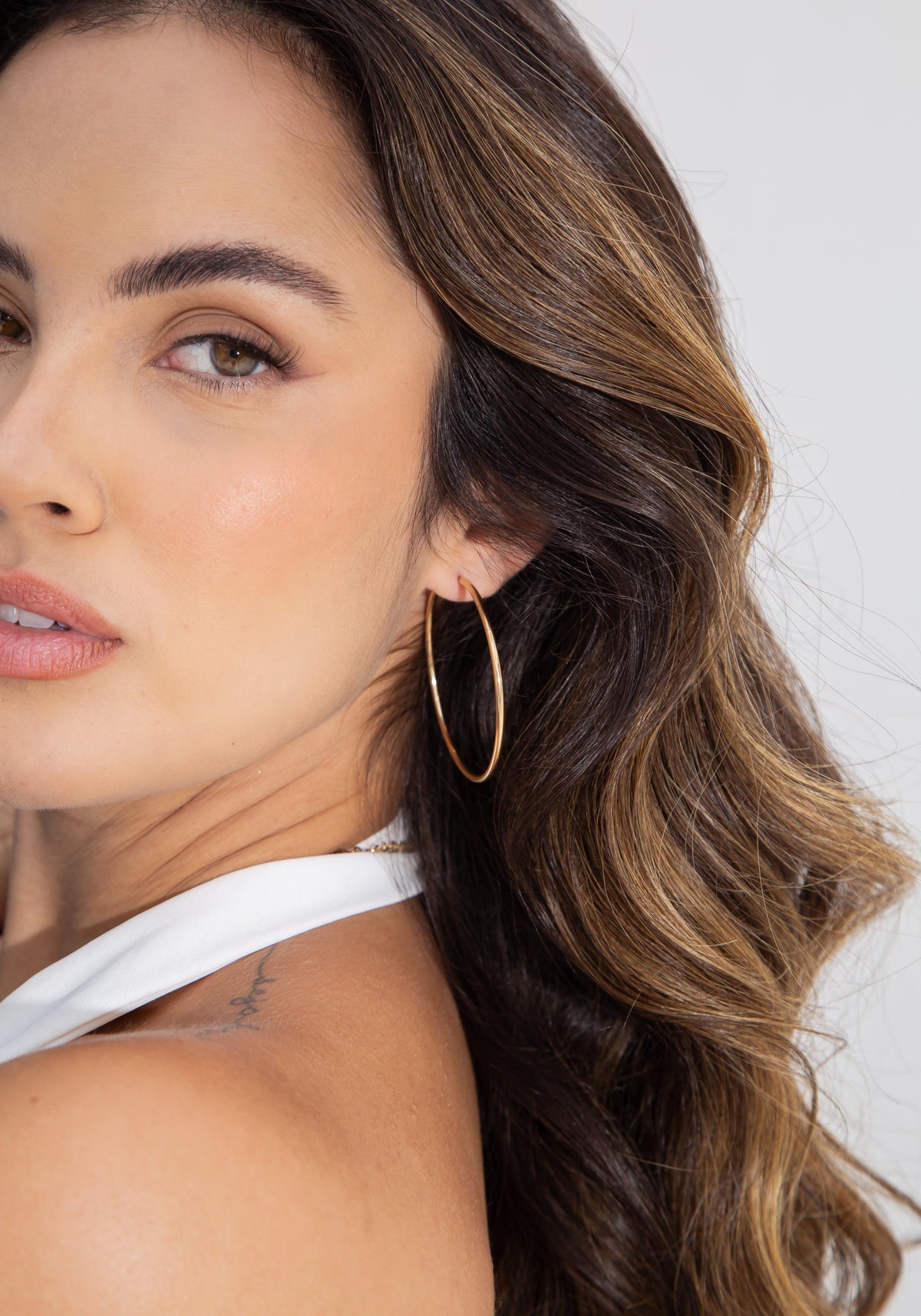 A woman with long brown hair poses with a large gold hoop earring.