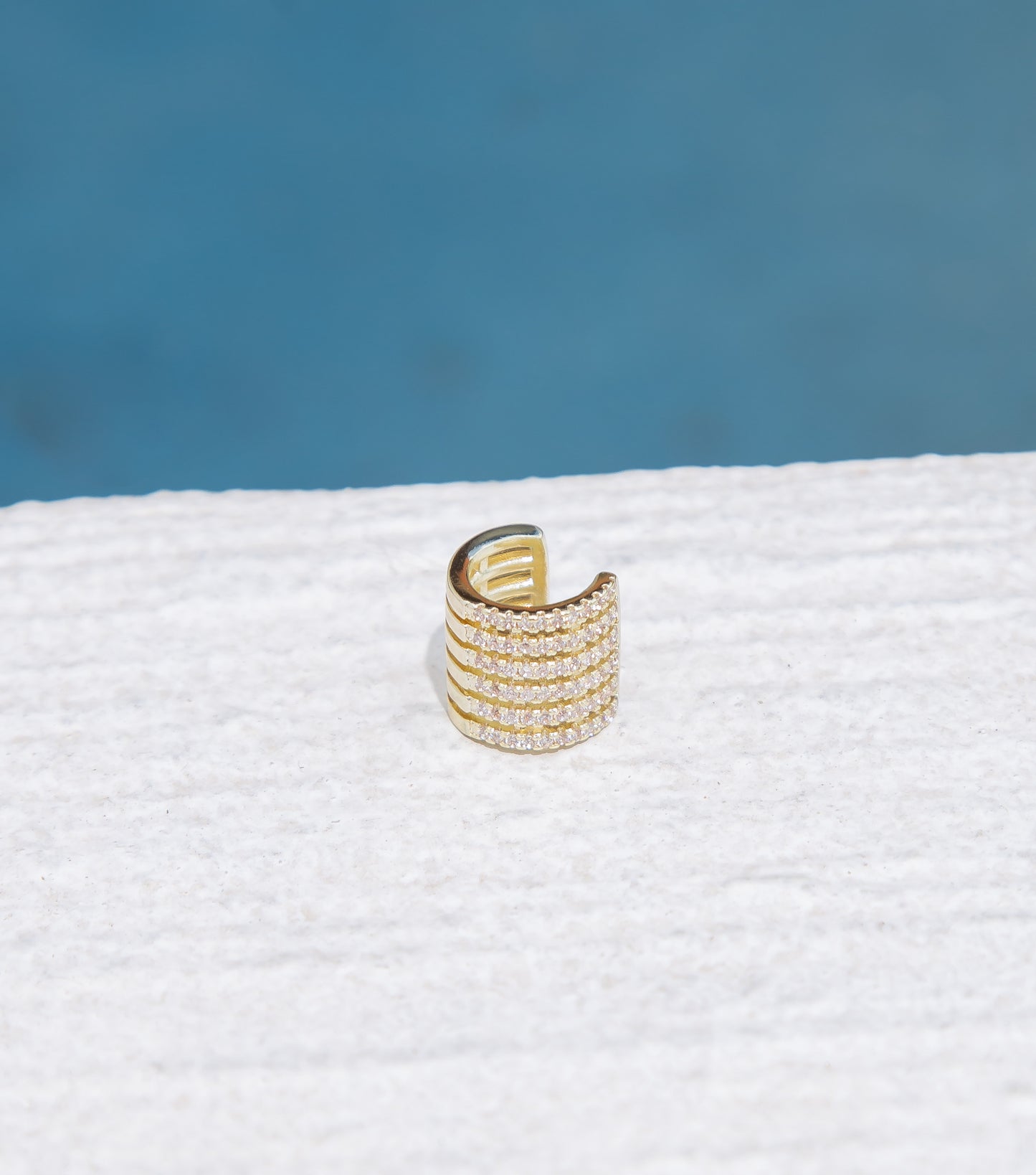 A shimmering gold ear cuff sparkles against a textured white surface.