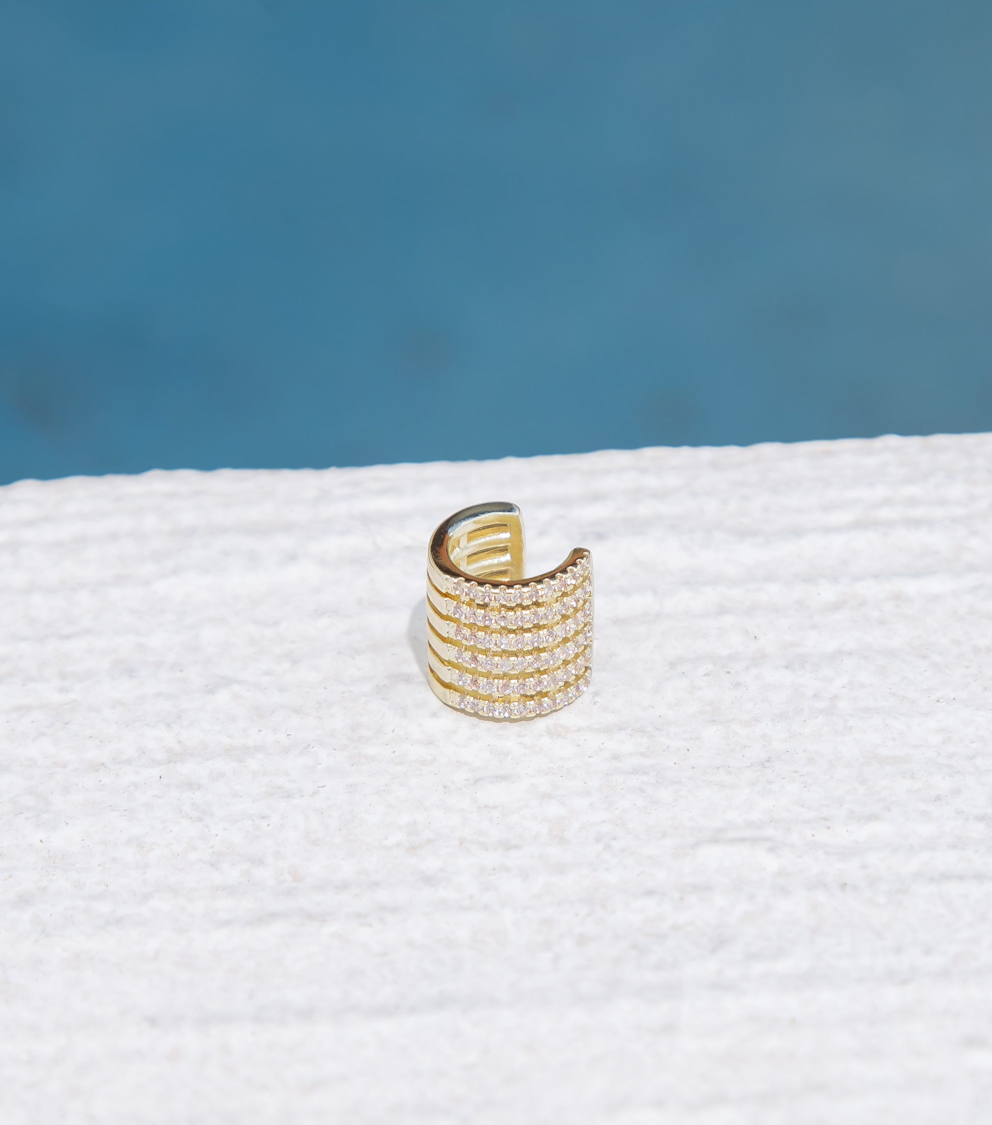 A shimmering gold ear cuff sparkles against a textured white surface.