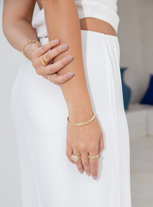 A woman wearing a white outfit showcases an array of elegant gold rings and bracelets on her arms.