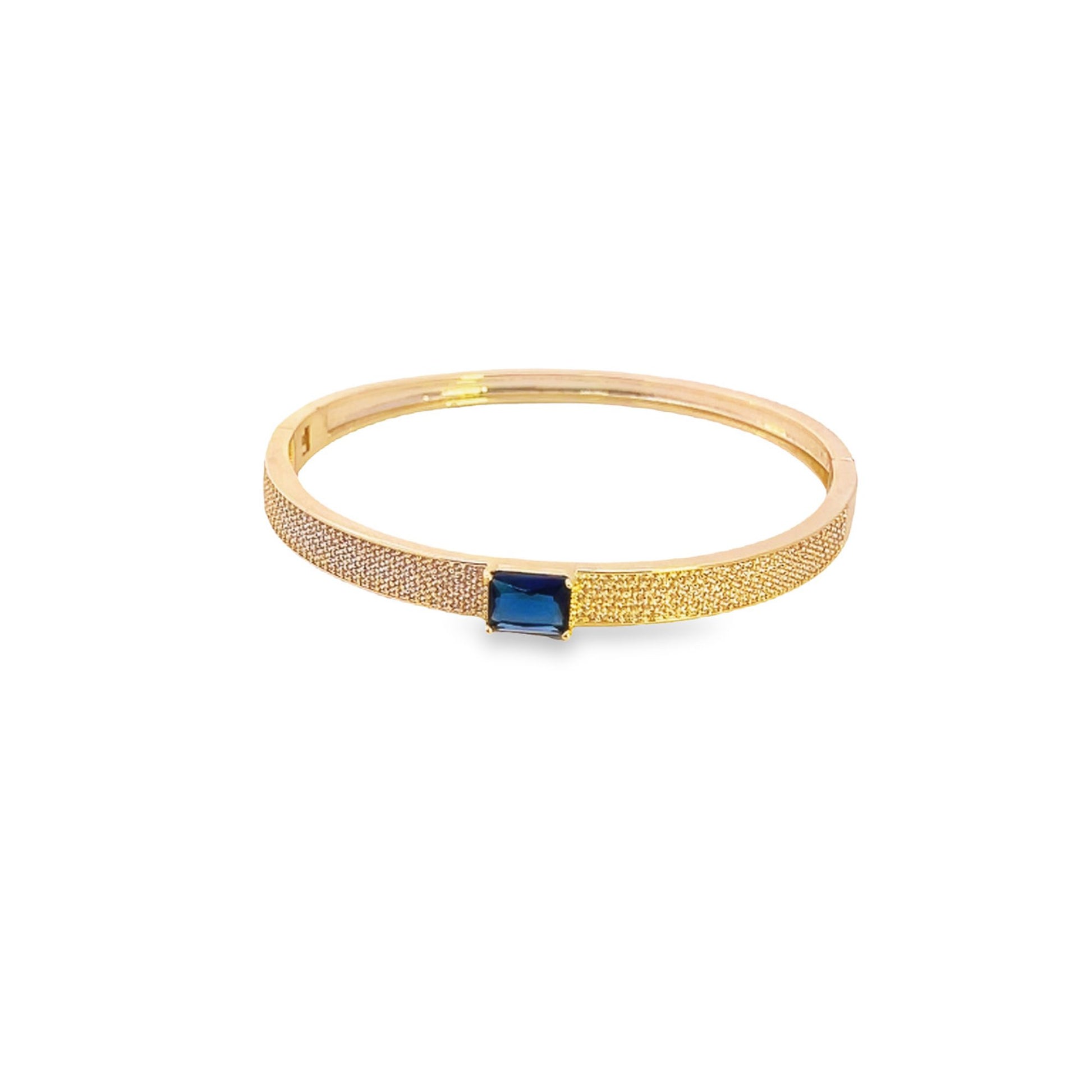 A gold bangle bracelet showcases a sparkling pave band centered with an emerald-cut blue sapphire gemstone.