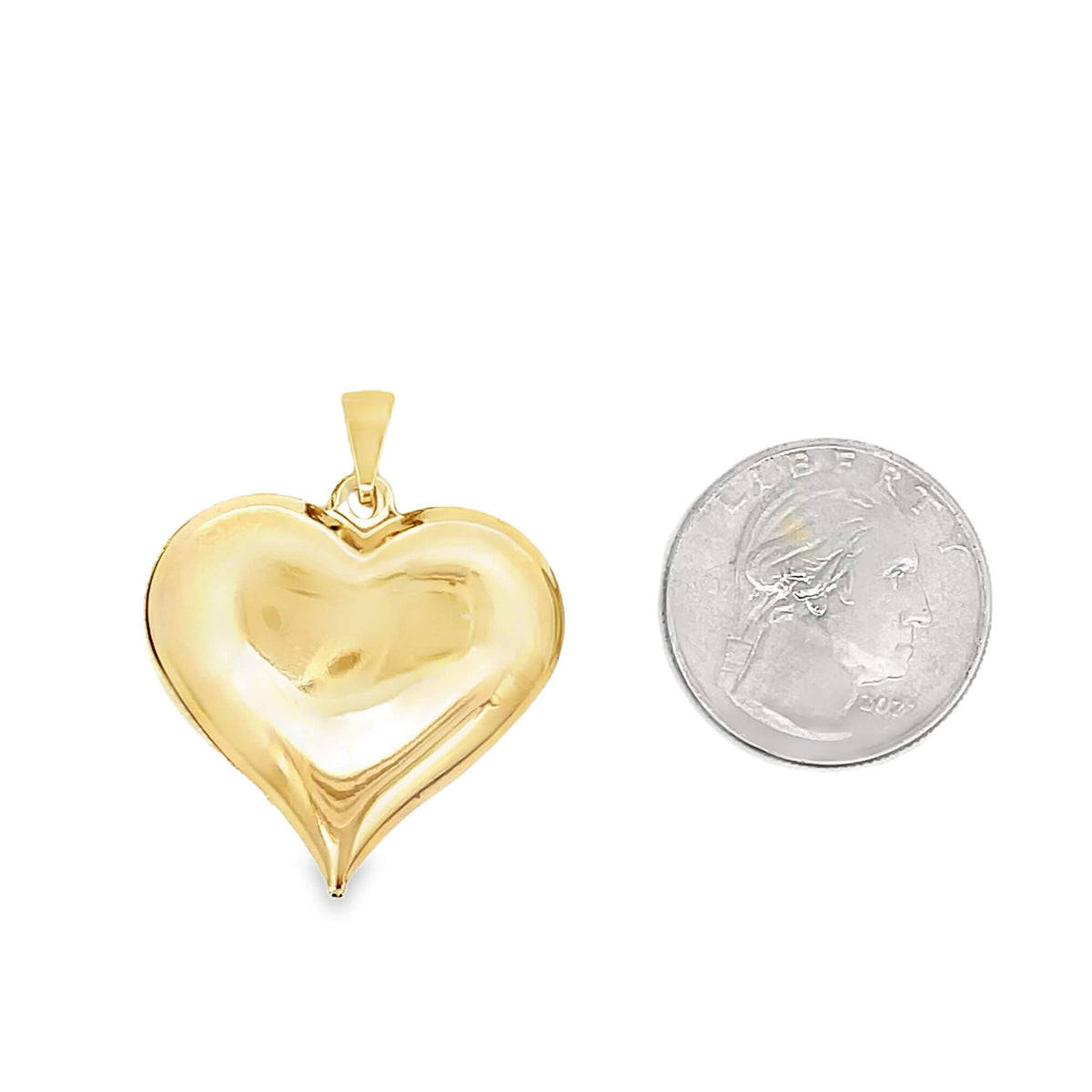 A polished yellow gold puffy heart pendant rests beside a US quarter for size comparison on a white background.