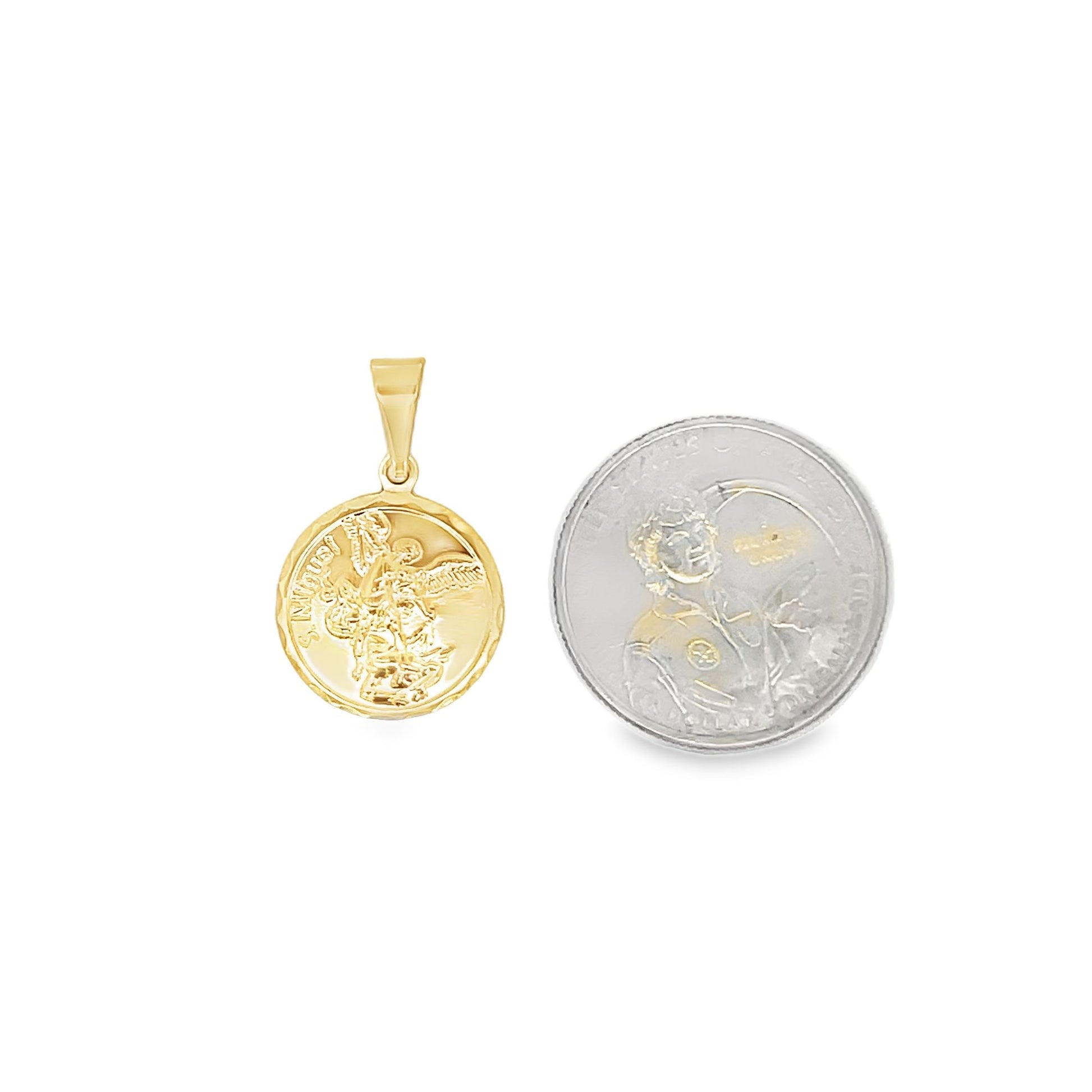 A gold Saint Michael pendant rests next to a coin for size comparison on a white background.