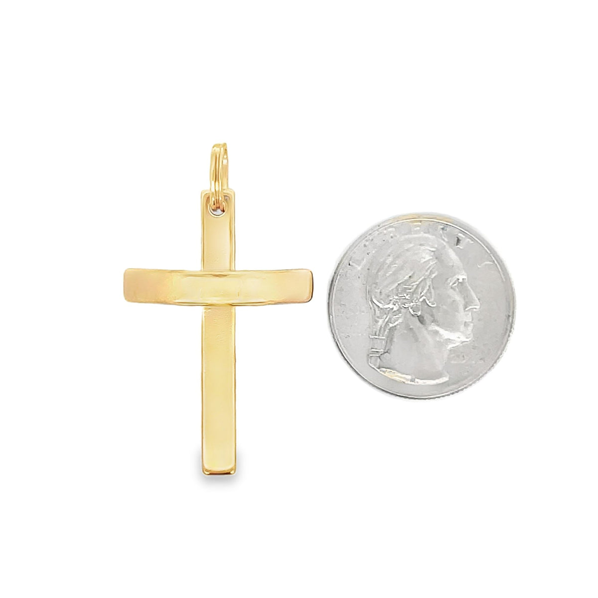 A polished yellow gold cross pendant rests next to a US quarter coin for size comparison.