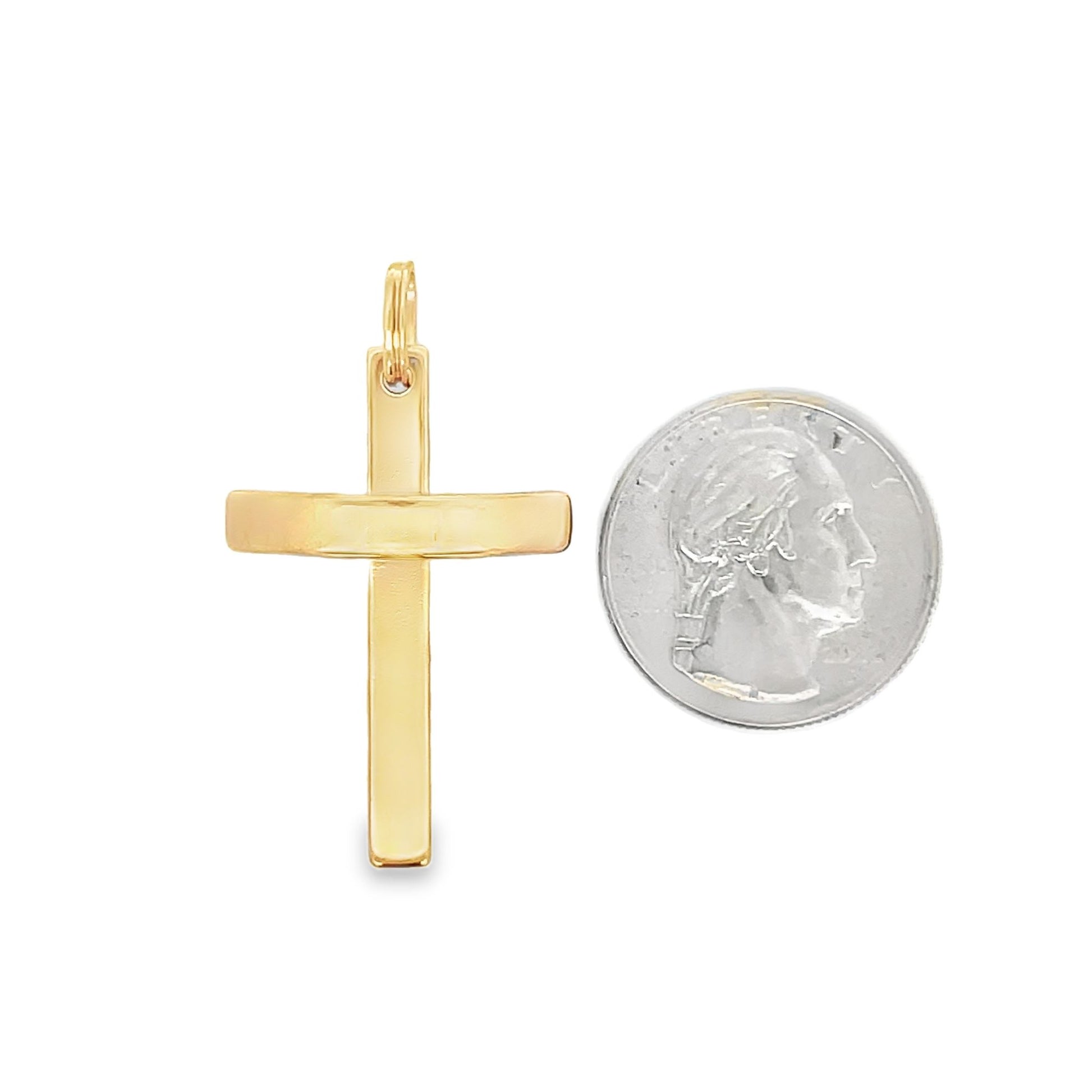 A polished yellow gold cross pendant rests next to a US quarter coin for size comparison.