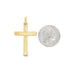 A polished yellow gold cross pendant rests next to a US quarter coin for size comparison.