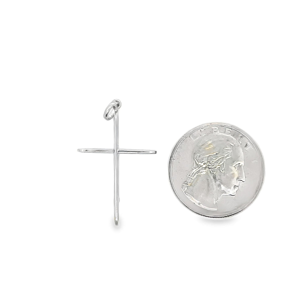 A sleek silver cross pendant lies next to a US quarter coin for scale.