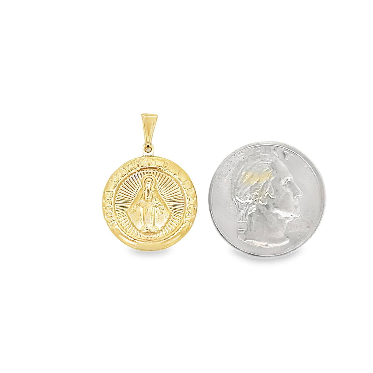 A gold Our Lady of Grace pendant rests next to a quarter for size comparison.