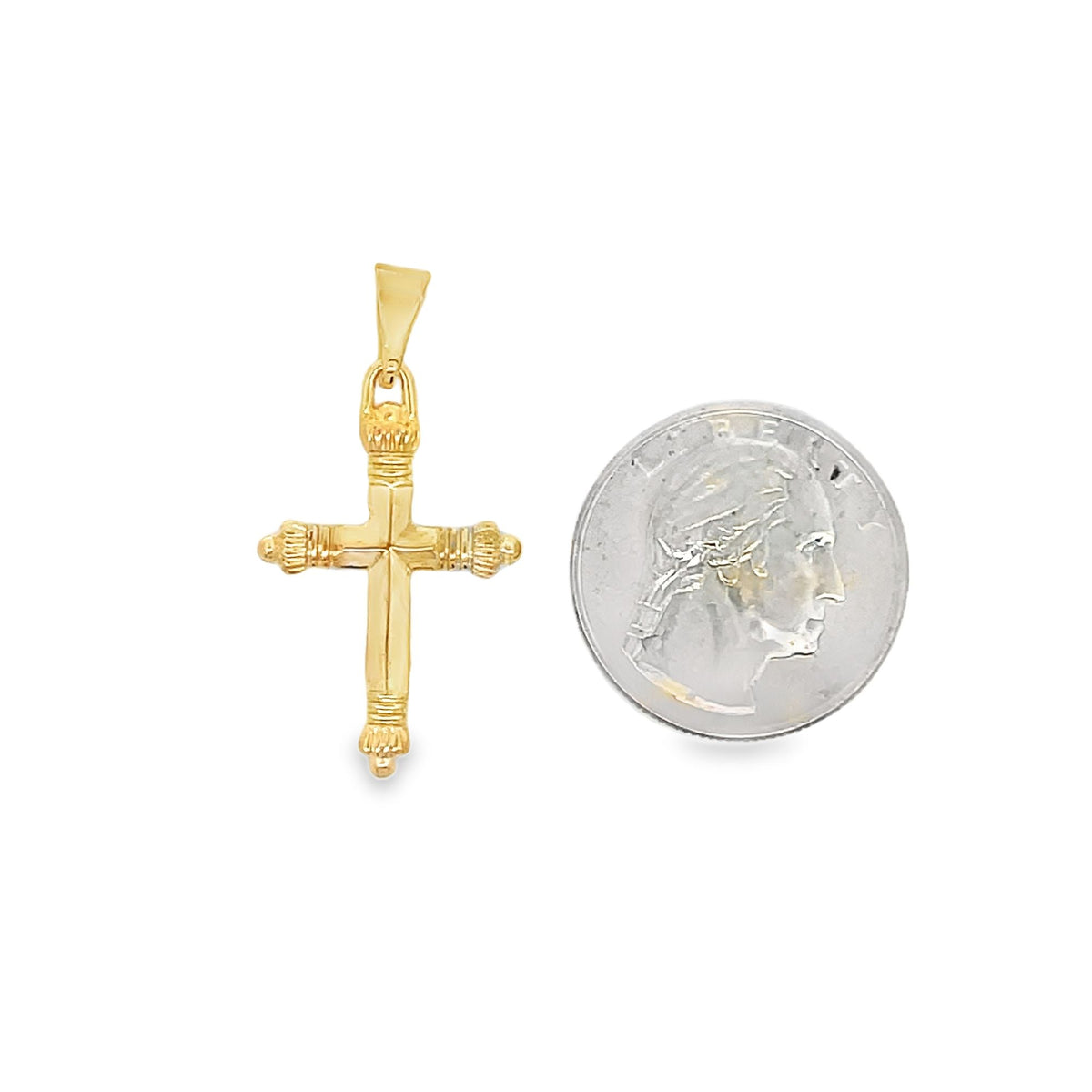 A detailed yellow gold cross pendant rests beside a US quarter for size comparison against a plain white background.