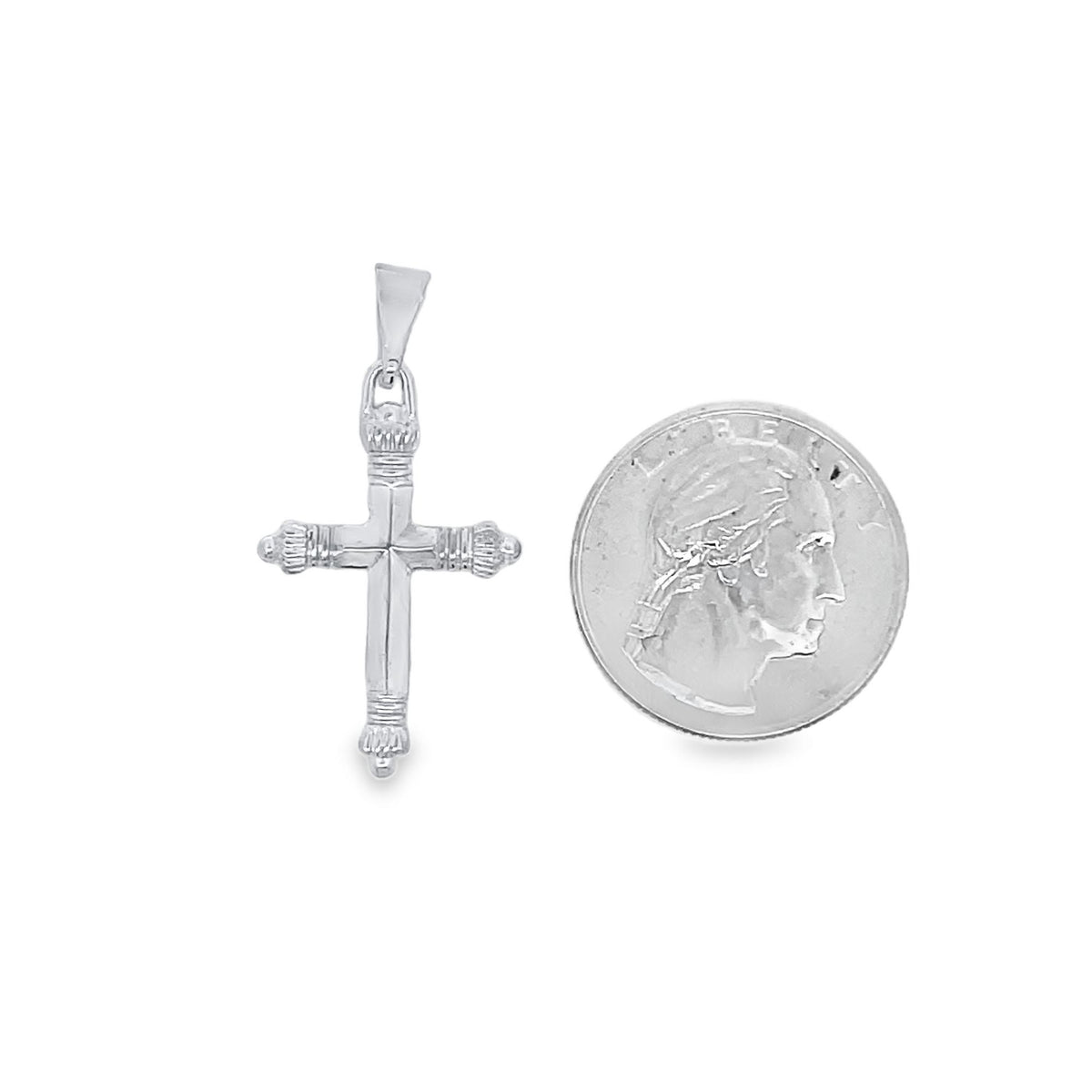 A silver cross pendant rests next to a US quarter coin to show its scale.