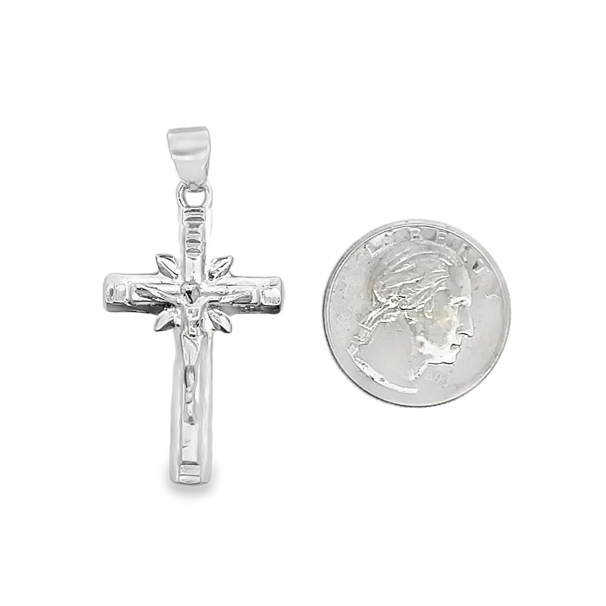 A shiny sterling silver crucifix pendant rests next to a US quarter coin to show its scale.