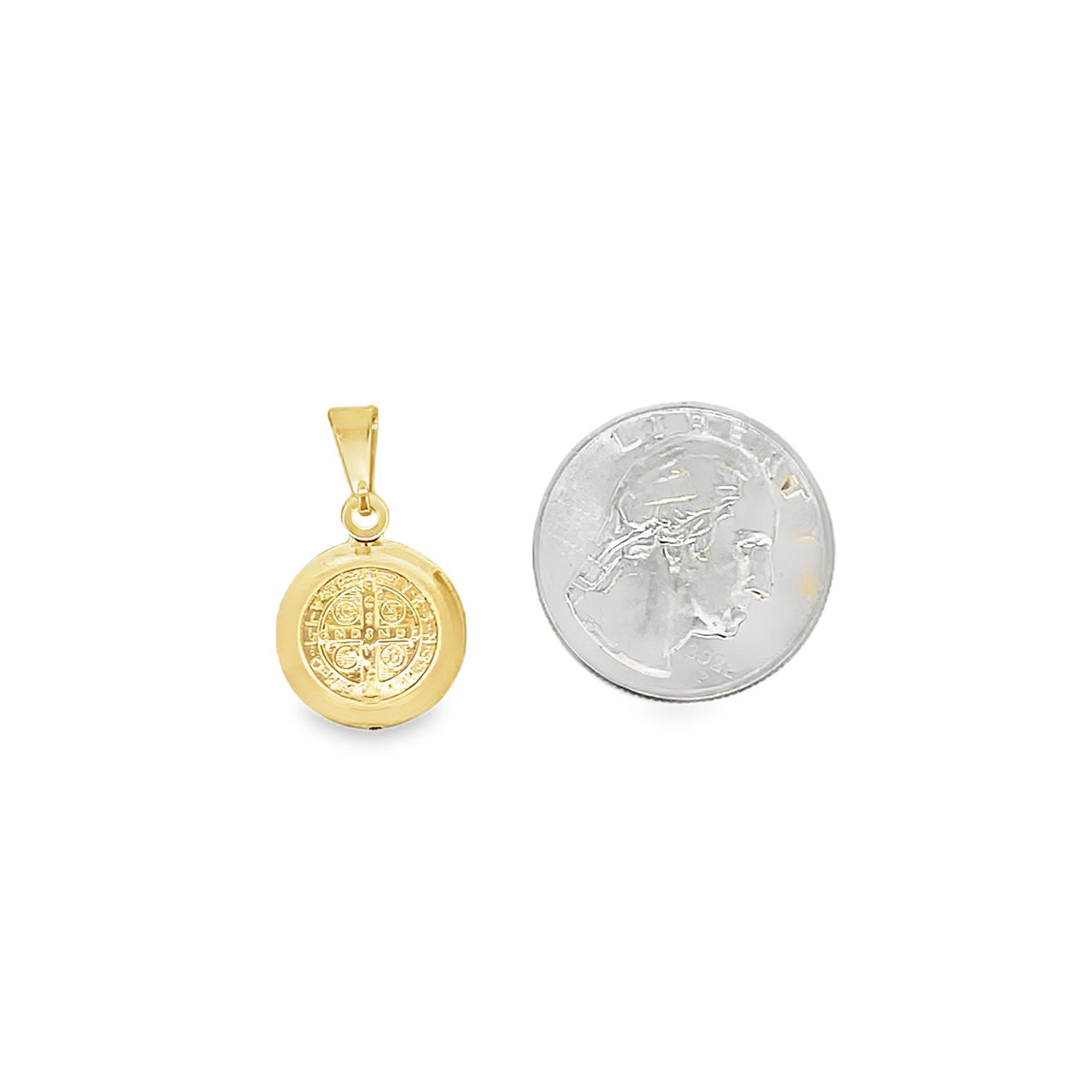 A gold Saint Benedict medallion pendant rests next to a US quarter for size comparison against a plain white background.